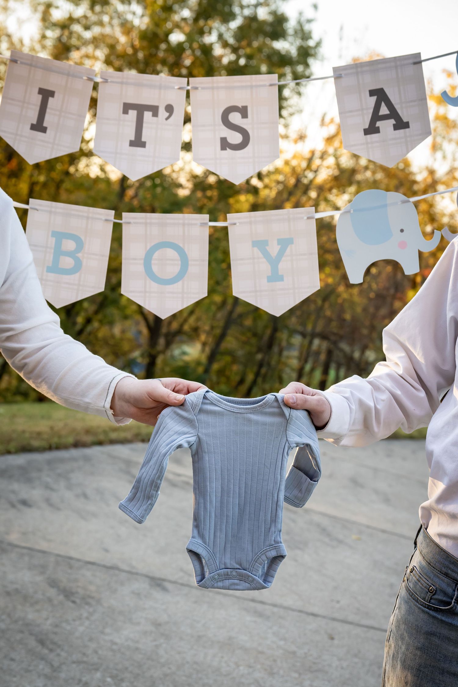 Baby clothes and 'It's a boy' banner hanging on a clothesline against a sunset background.