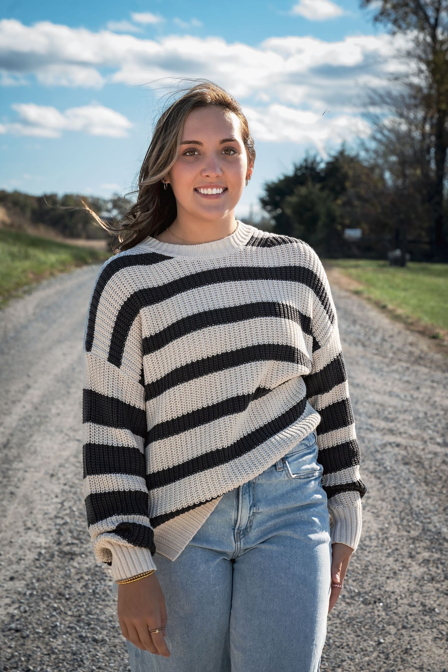 Person wearing striped sweater and jeans poses on country road with natural lighting.
