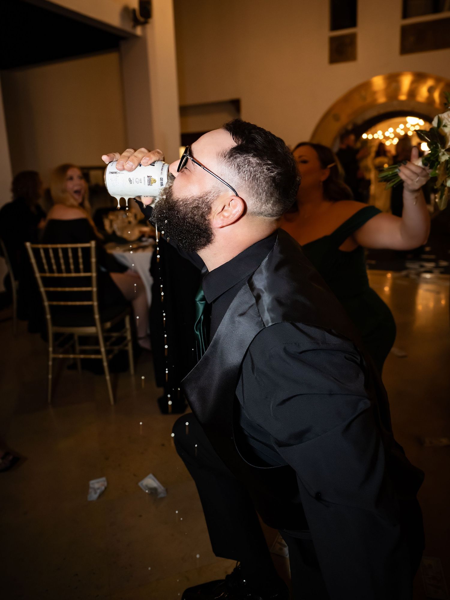 Wedding guest takes celebratory drink at dimly lit reception venue.