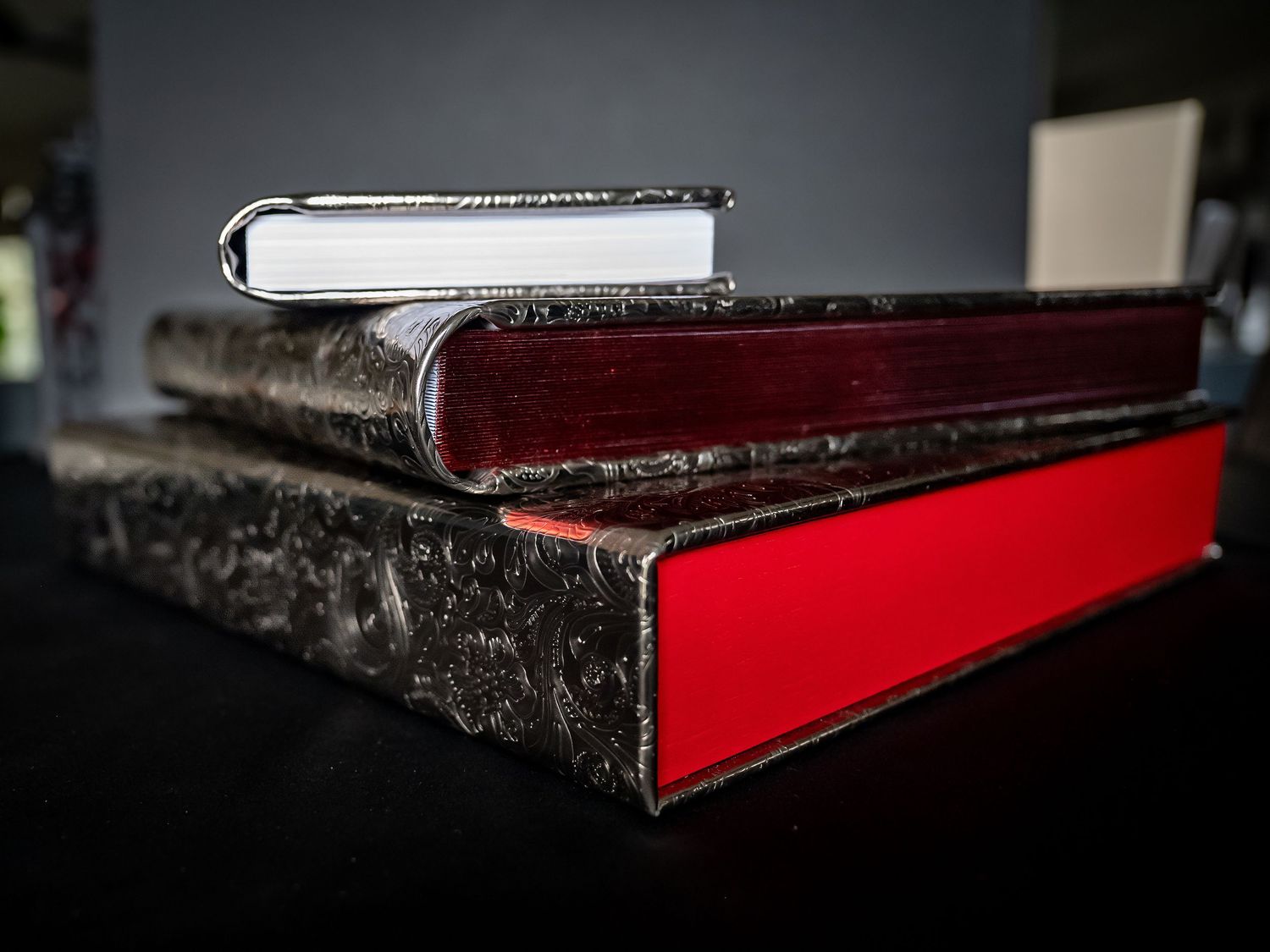 A black and red hardcover luxury album shown from multiple angles against a dark background.