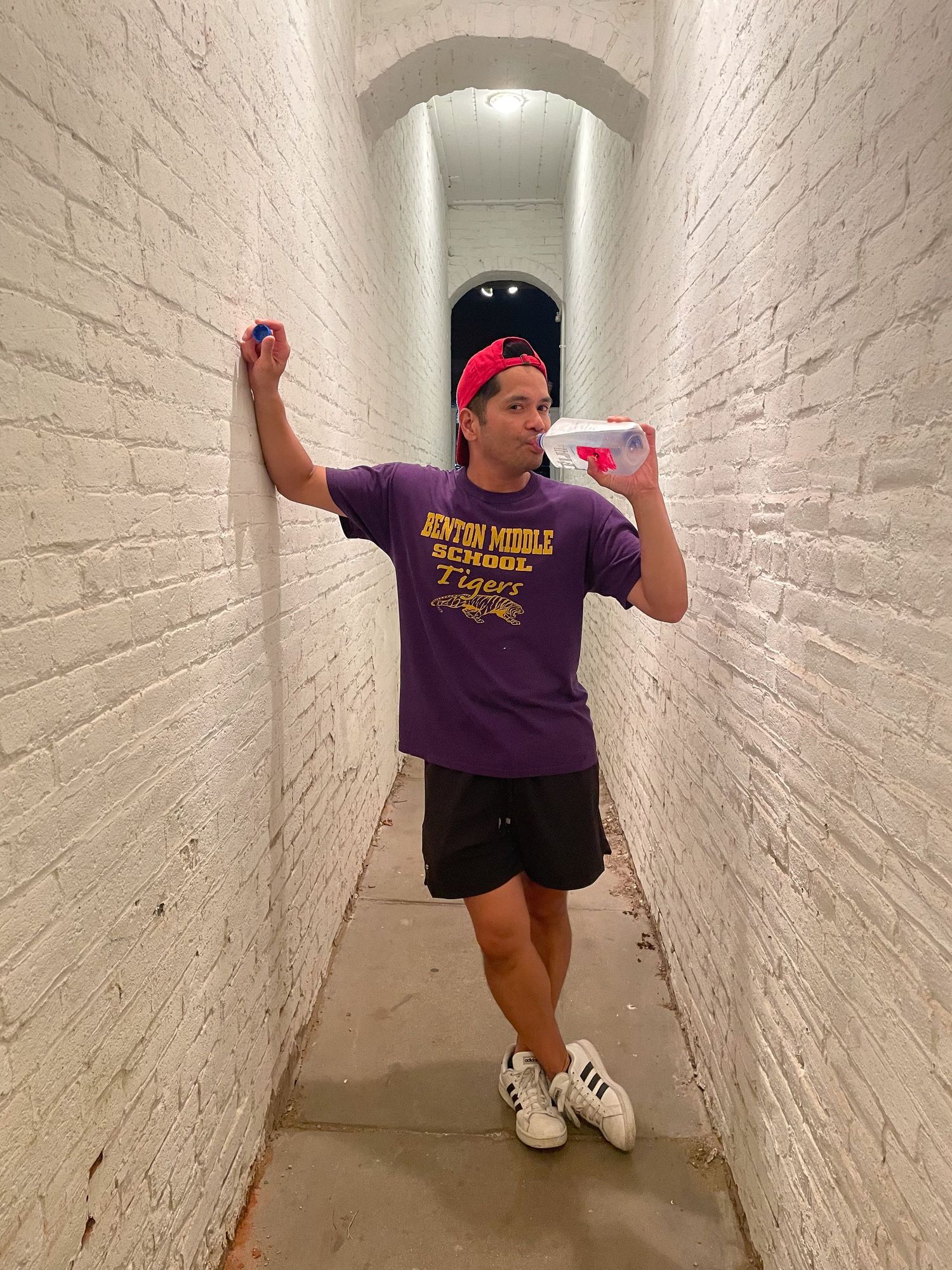 Young person in purple Benton Middle School Tigers shirt and red cap poses in white brick tunnel hallway.