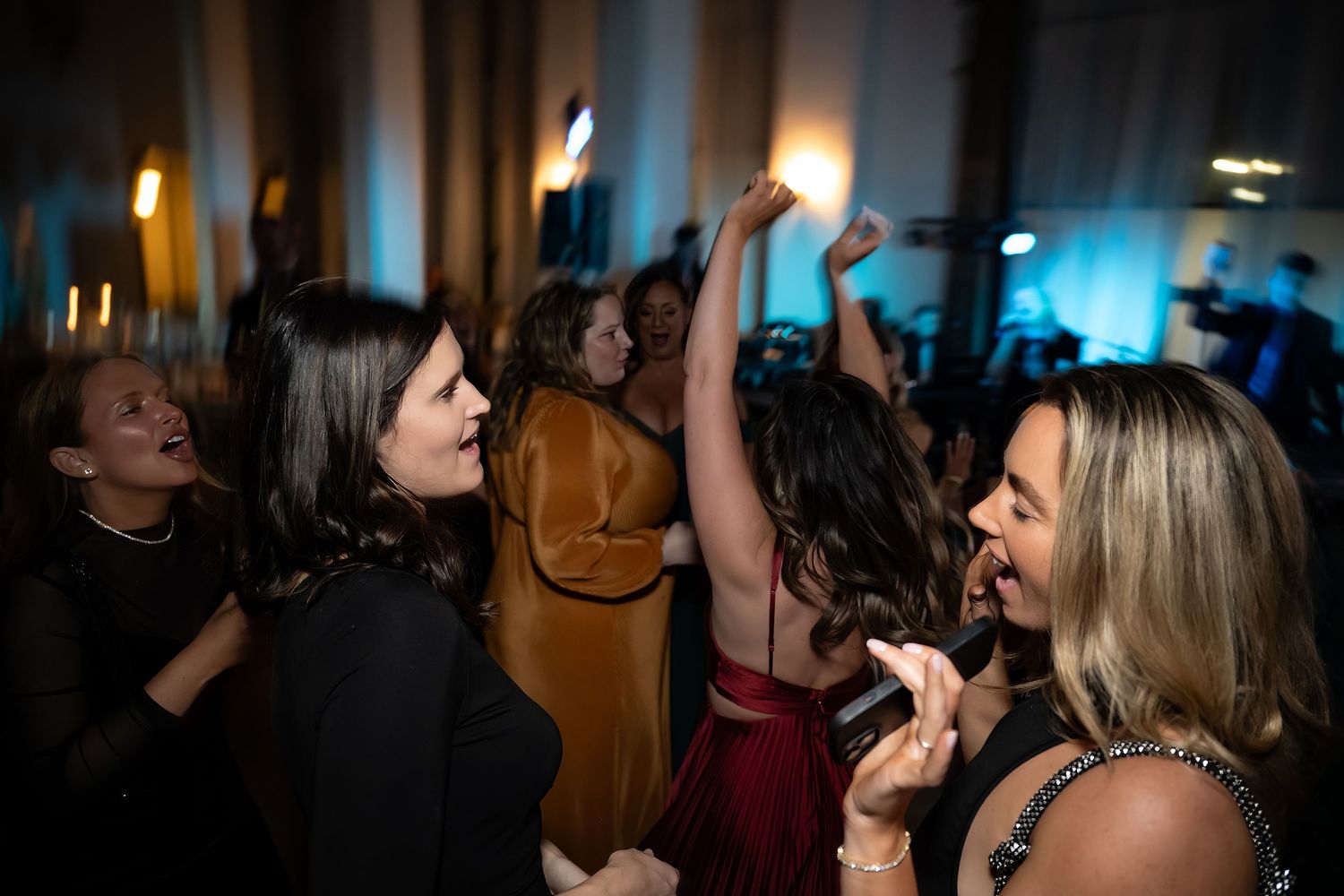Wedding guests dance and celebrate at evening reception with blue lighting effects.