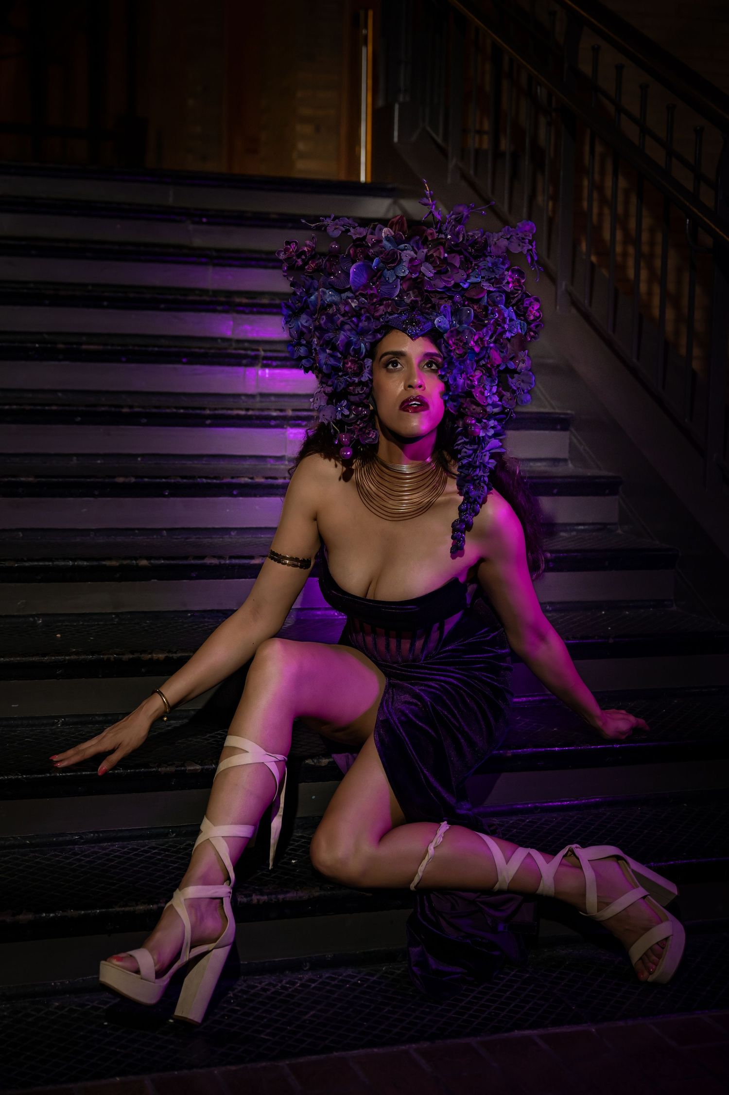 Dramatic pose on dark stairs with purple lighting and floral accessories.