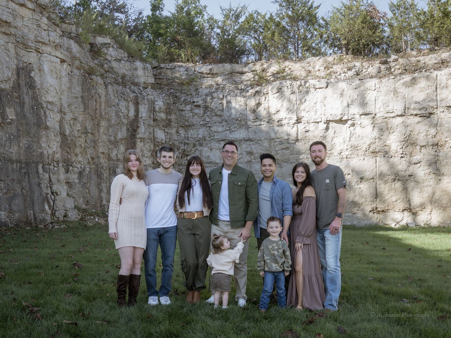 Family group portrait against stone wall backdrop in natural outdoor setting.
