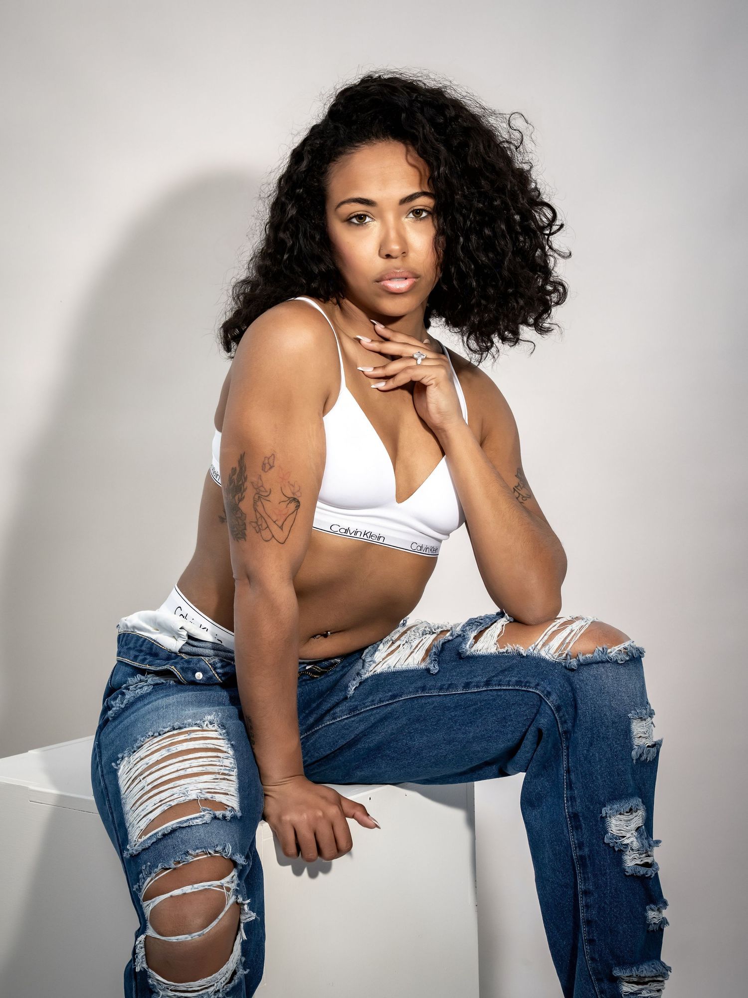 Fashion model wearing ripped jeans and white top poses against white background in casual photoshoot series.