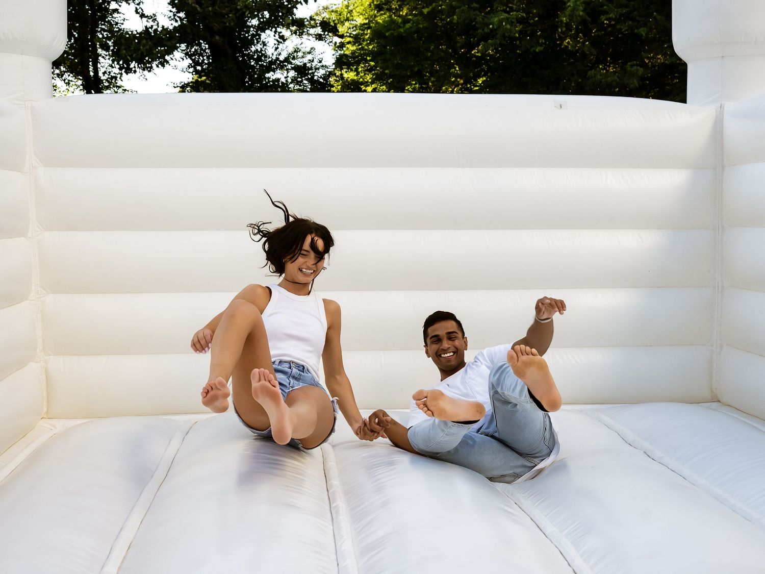 Two people laughing and jumping in a white bounce house outdoors.