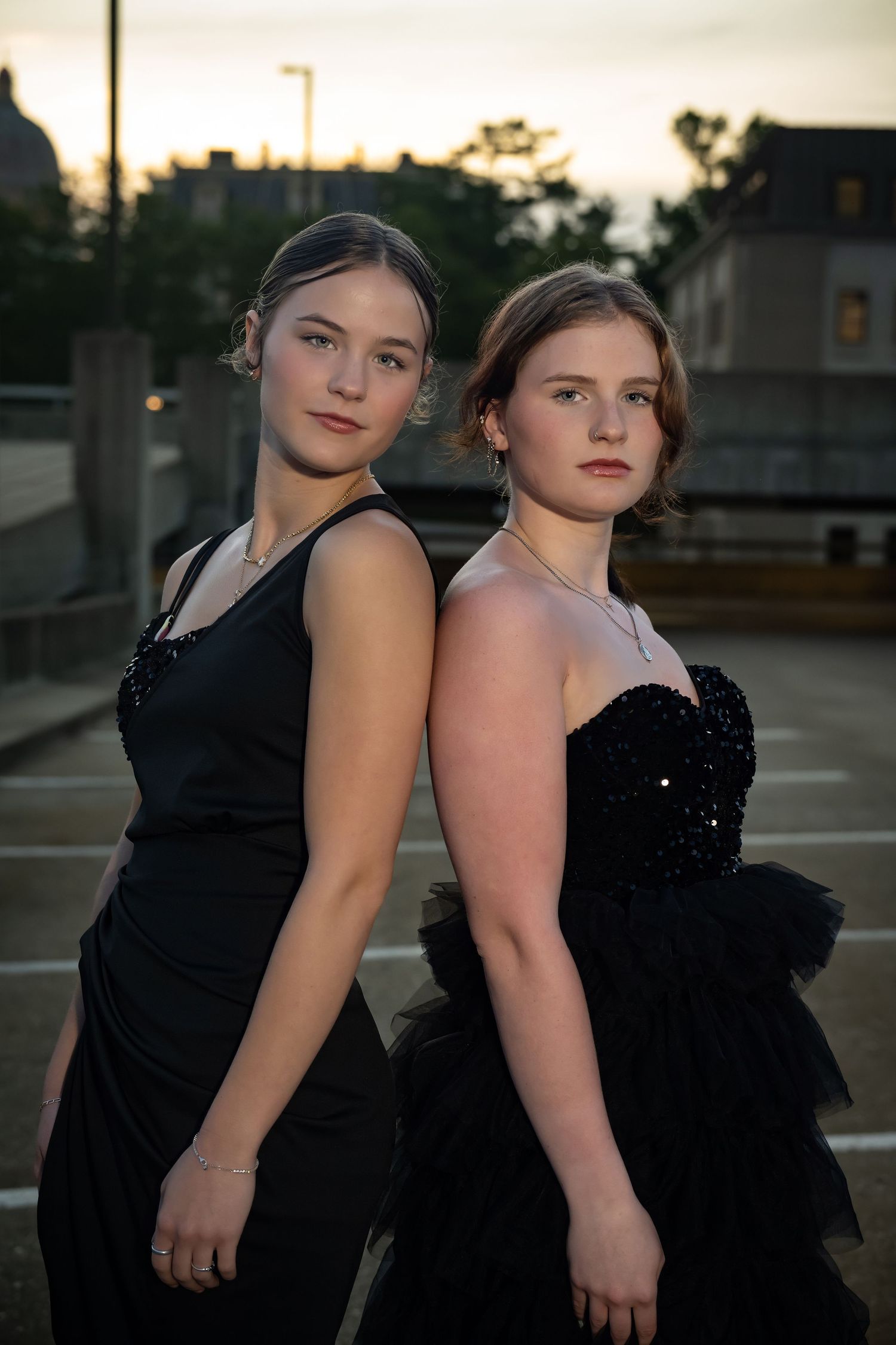 Two friends in black formal dresses pose together at sunset for portraits.