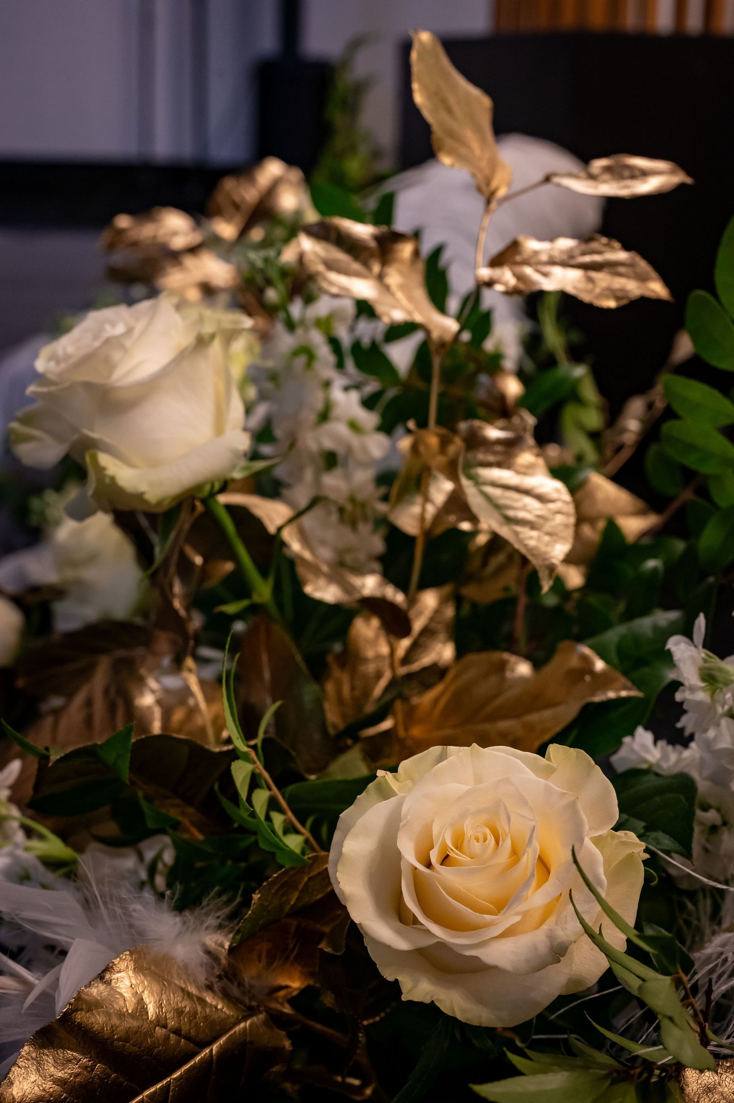 Cream colored roses with gold-painted leaves in romantic wedding floral arrangement.