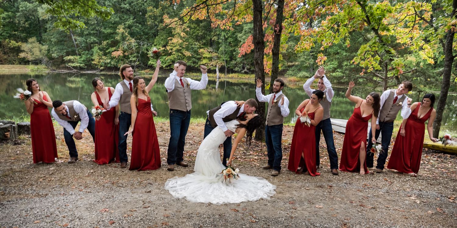 Wedding party in burgundy and white attire poses together in a natural outdoor setting.