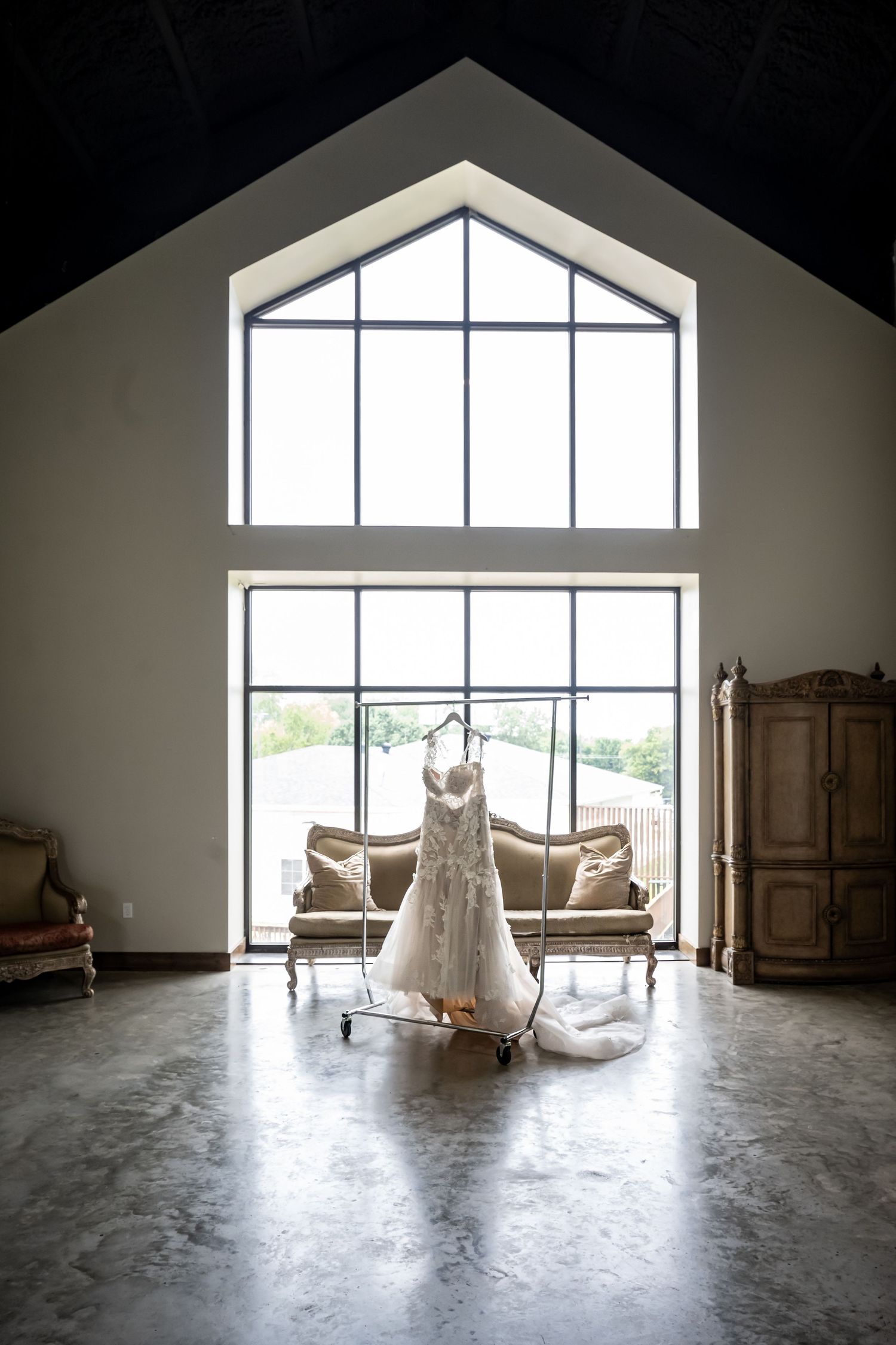 A wedding dress displayed in a bright room with large windows and elegant furniture.
