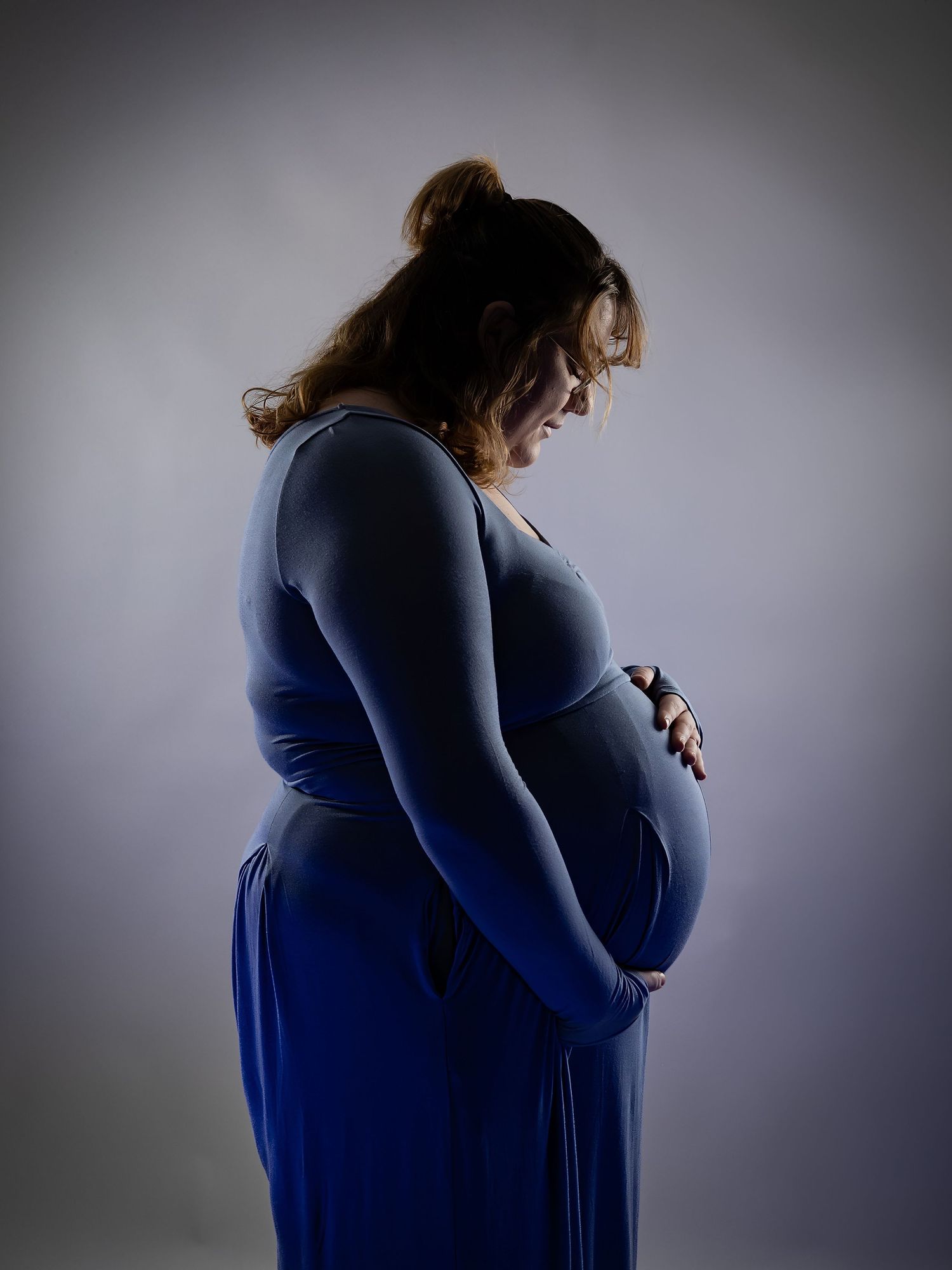 Side view silhouette of pregnant woman in blue dress against gray background.