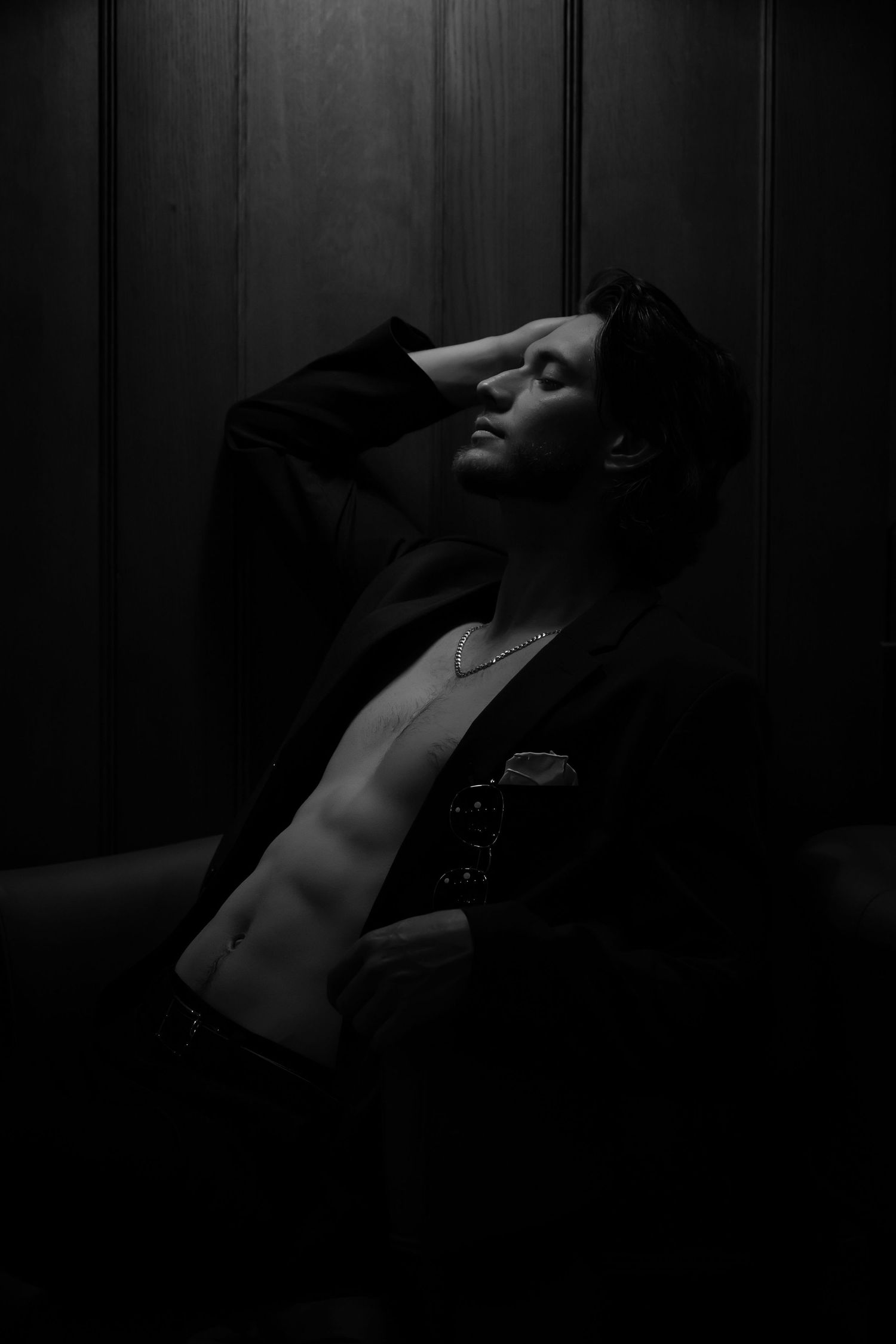 Silhouette of person leaning back against dark paneled wall in low light.