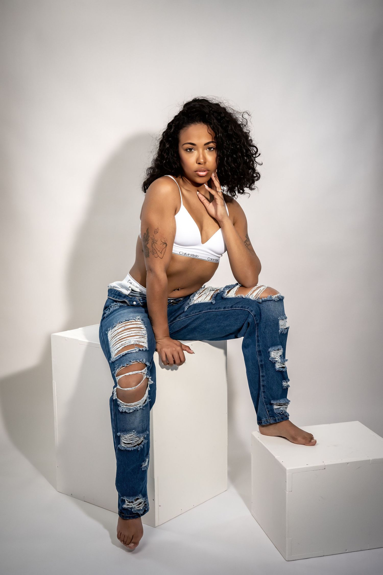 Studio fashion portrait of model in distressed jeans and white top on white blocks.