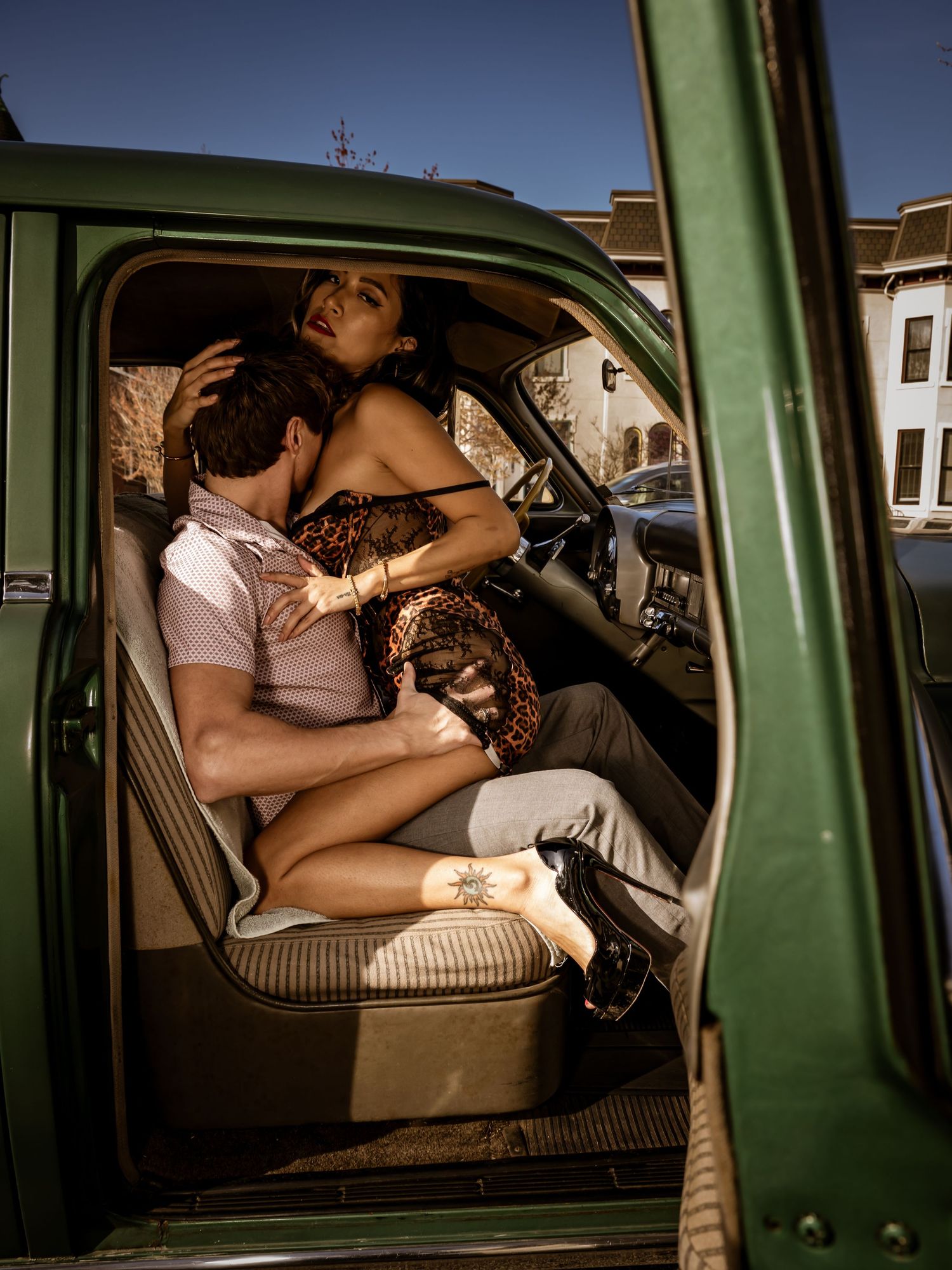 A couple embracing intimately inside a vintage green truck parked on a sunny street.
