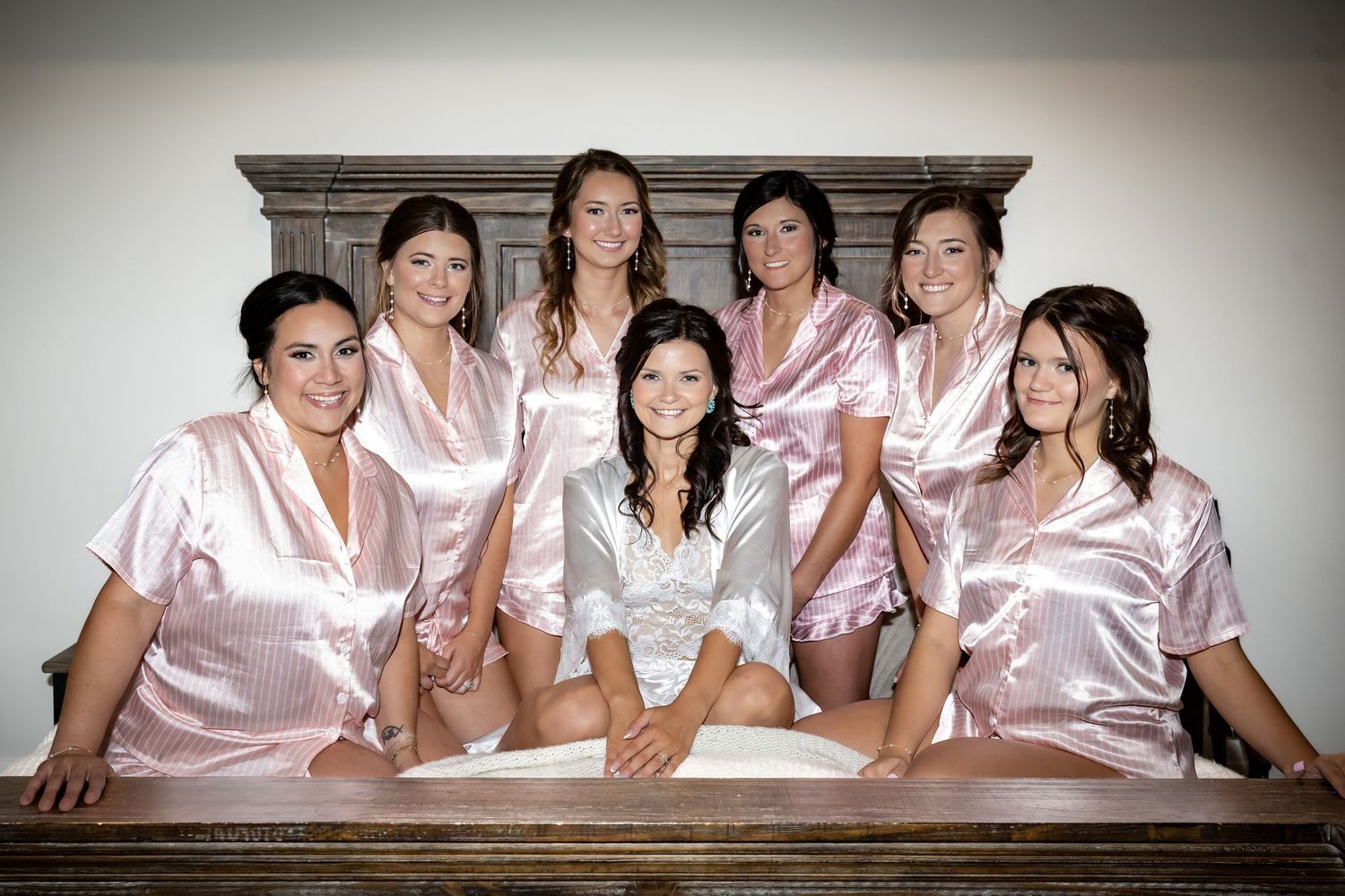 Bridesmaids in pink satin robes gather around wooden table during wedding preparations.