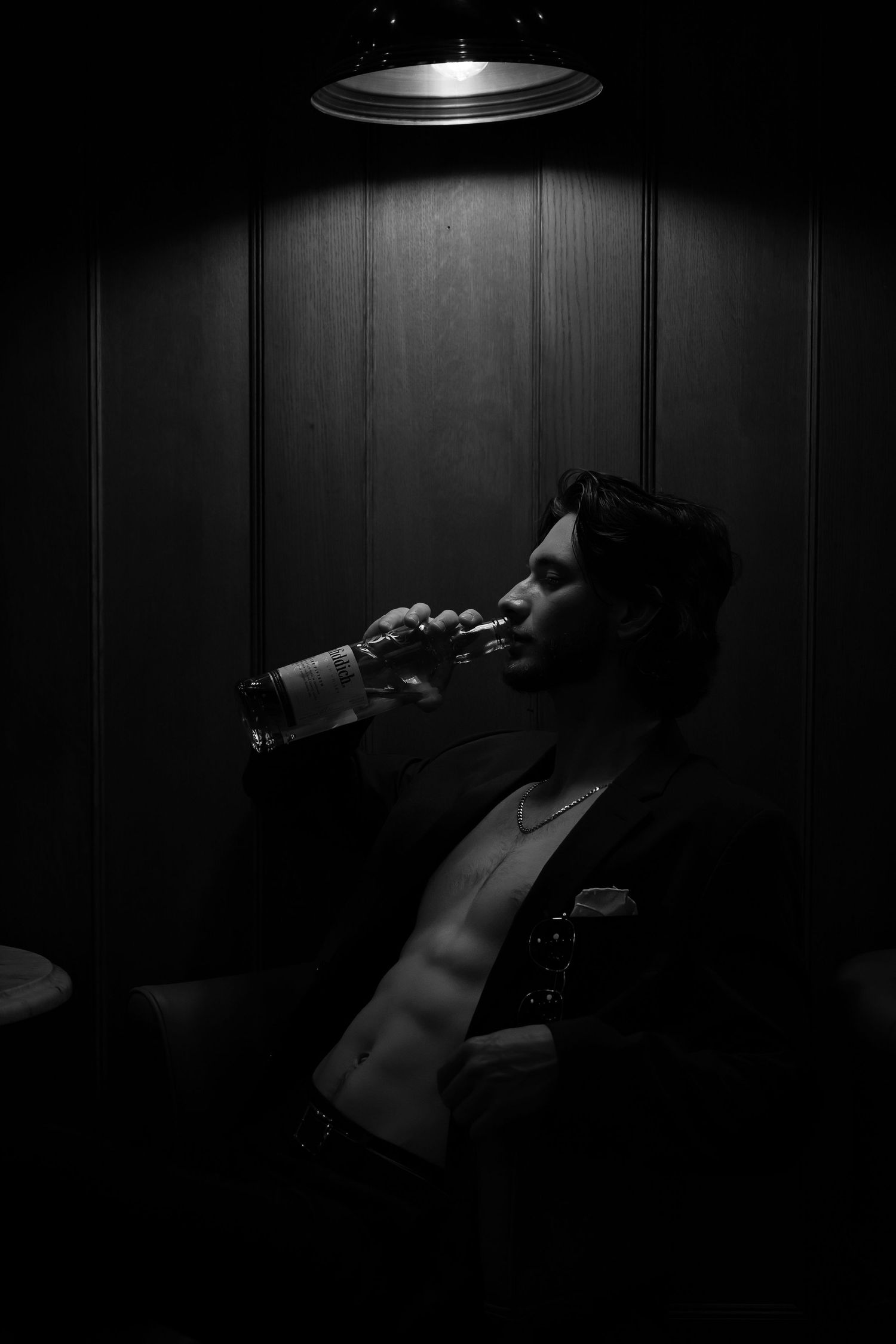 Dramatic black and white photo of someone drinking from a bottle in dark lighting.