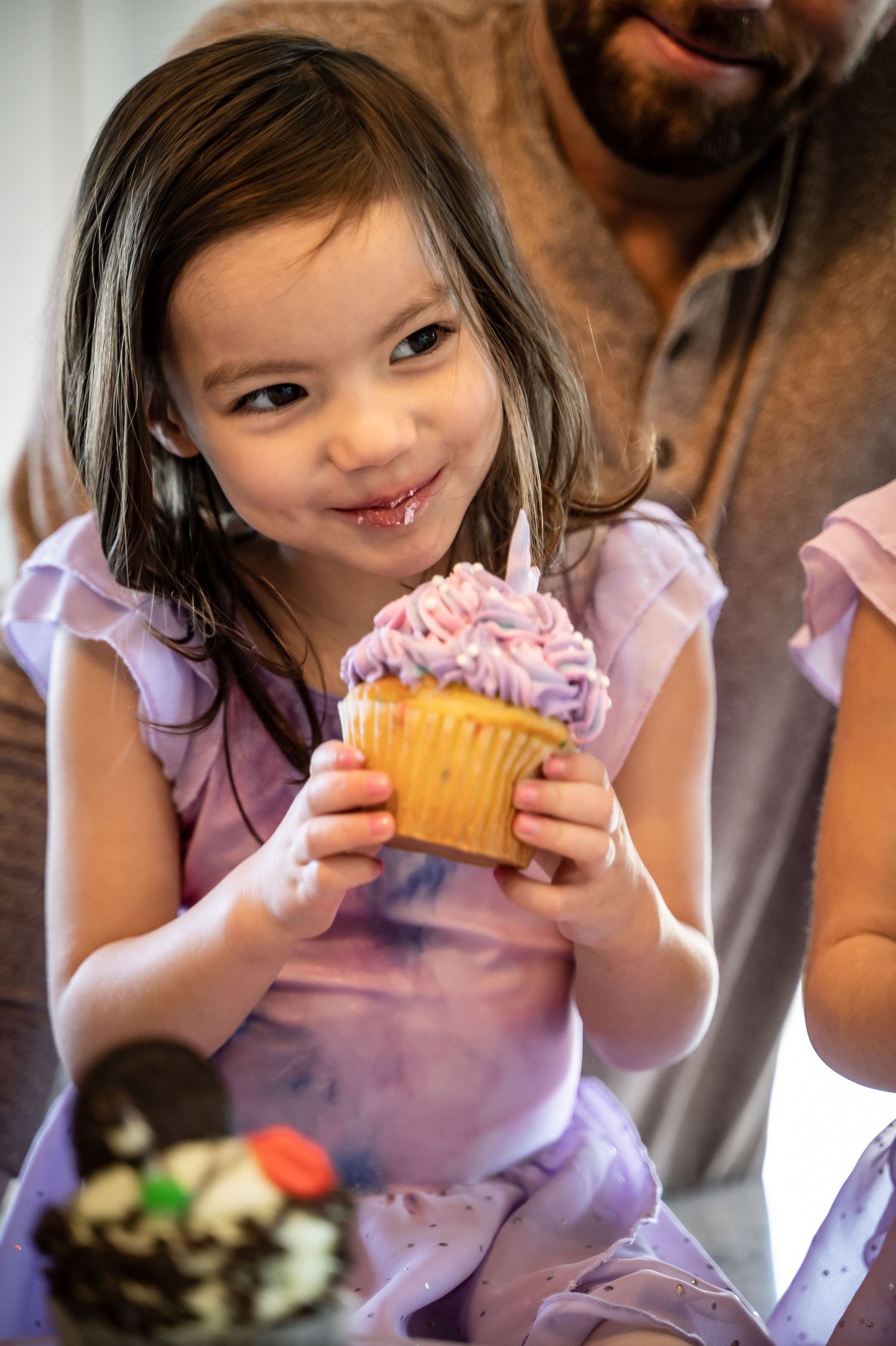 Child in purple shirt enjoying a cupcake with delighted expressions.