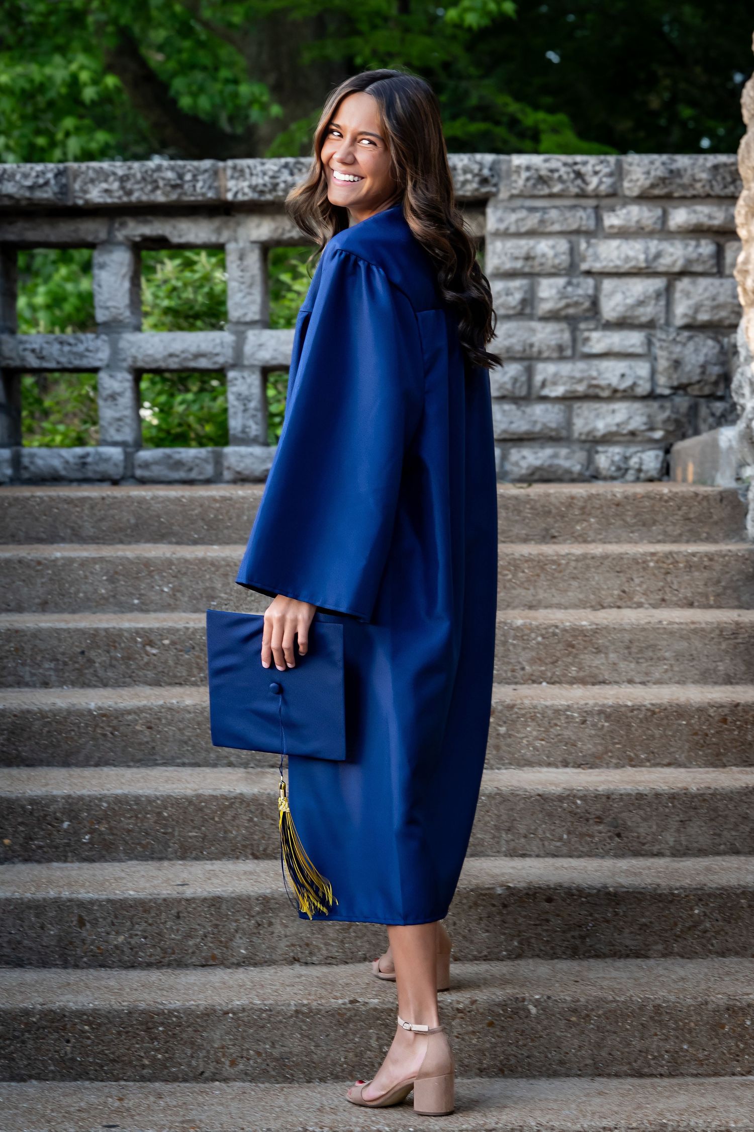 Playful graduation portraits on concrete steps with a navy blue academic gown.