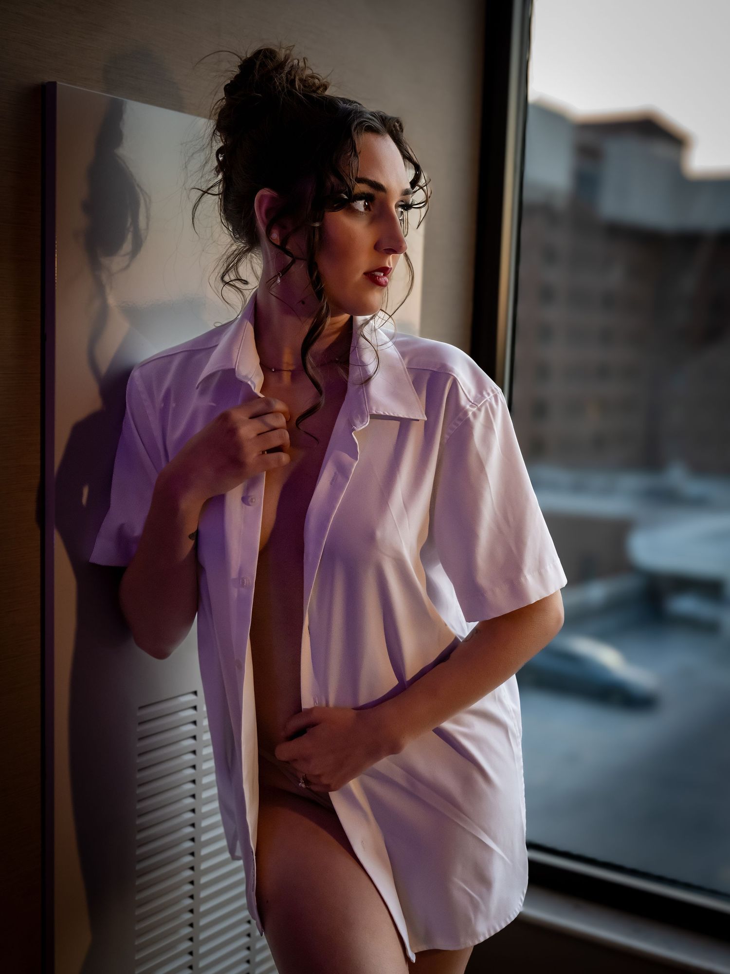 Artistic boudoir photo of model in oversized white shirt by window.