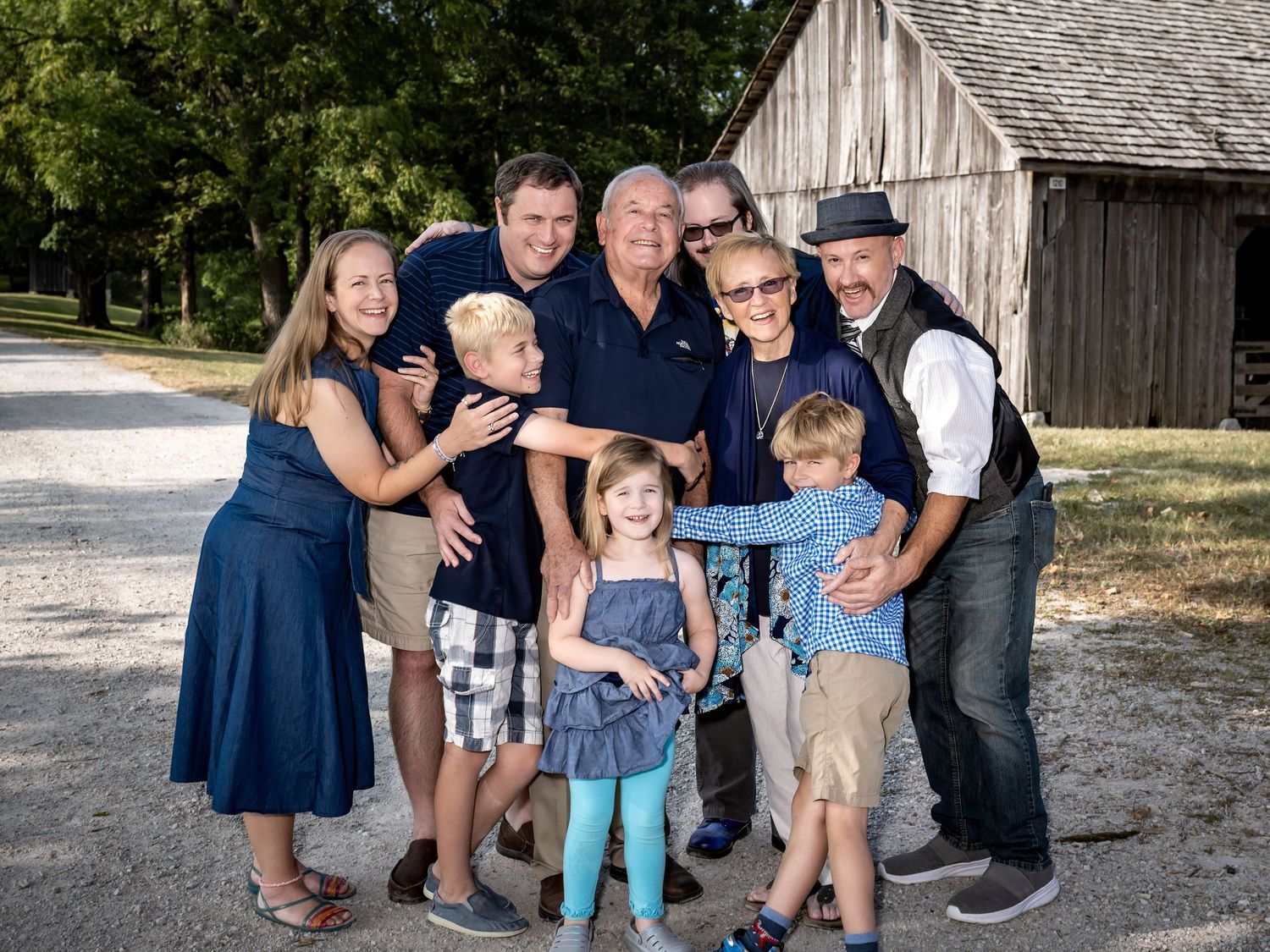 Multi-generational family gathering poses together in front of rustic barn building.