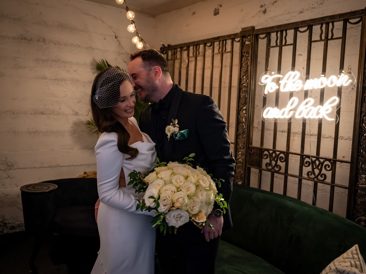 Romantic couple shares intimate moment with white floral bouquet in dimly lit venue.