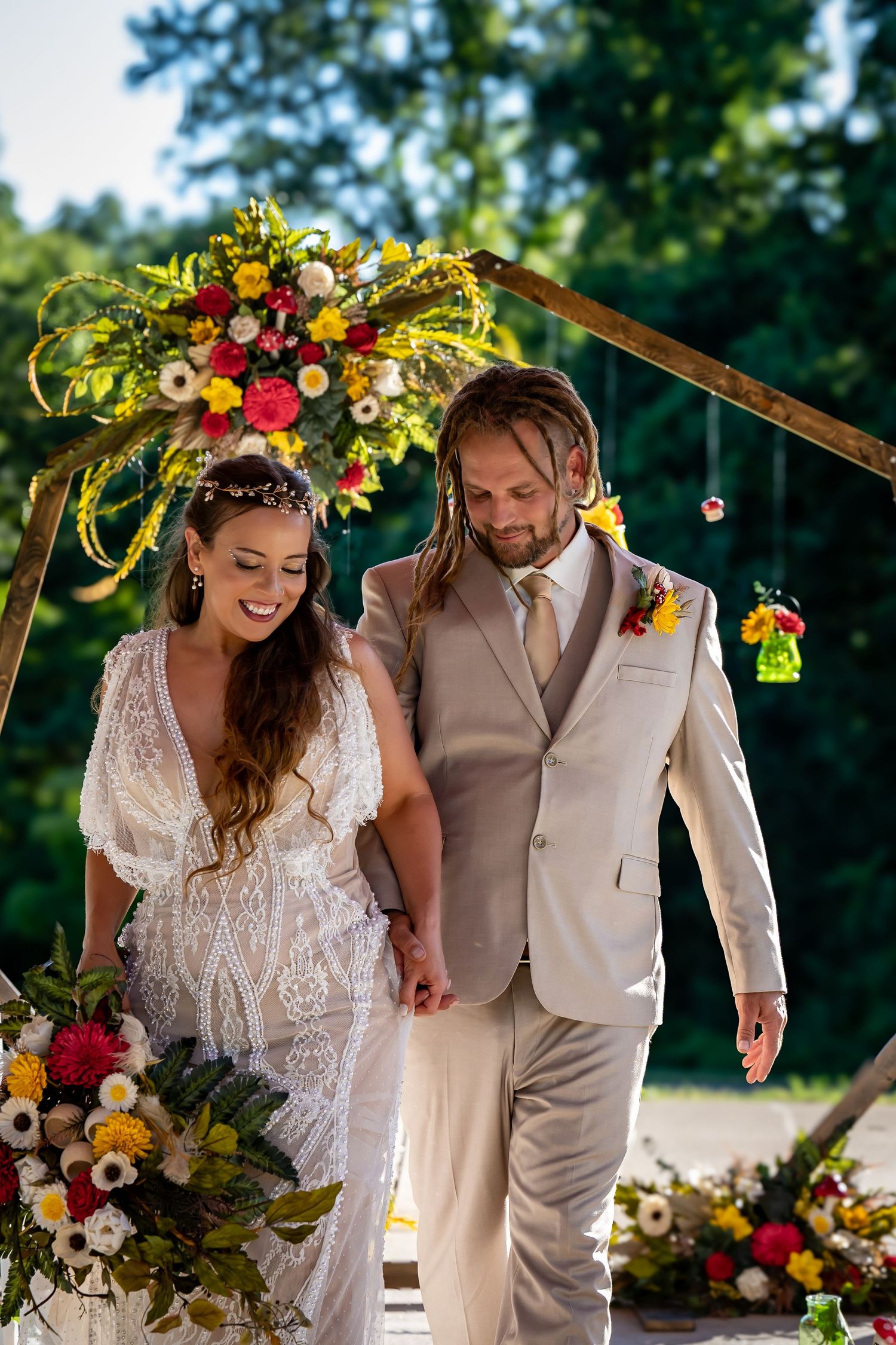 A romantic outdoor wedding ceremony with floral arch decorations and sunlit greenery in the background.