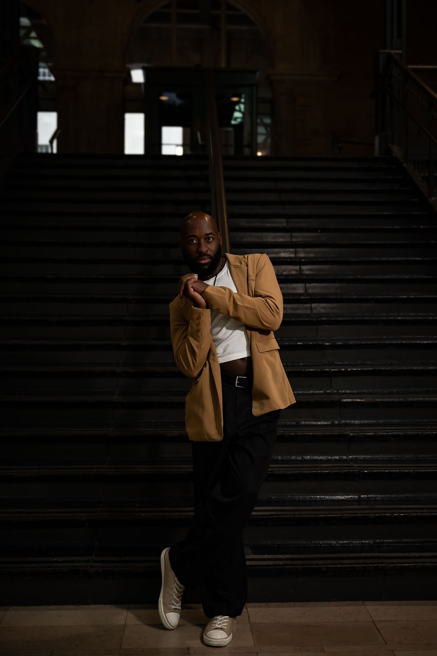 Person in tan coat sitting on dark stairs in moody lighting.