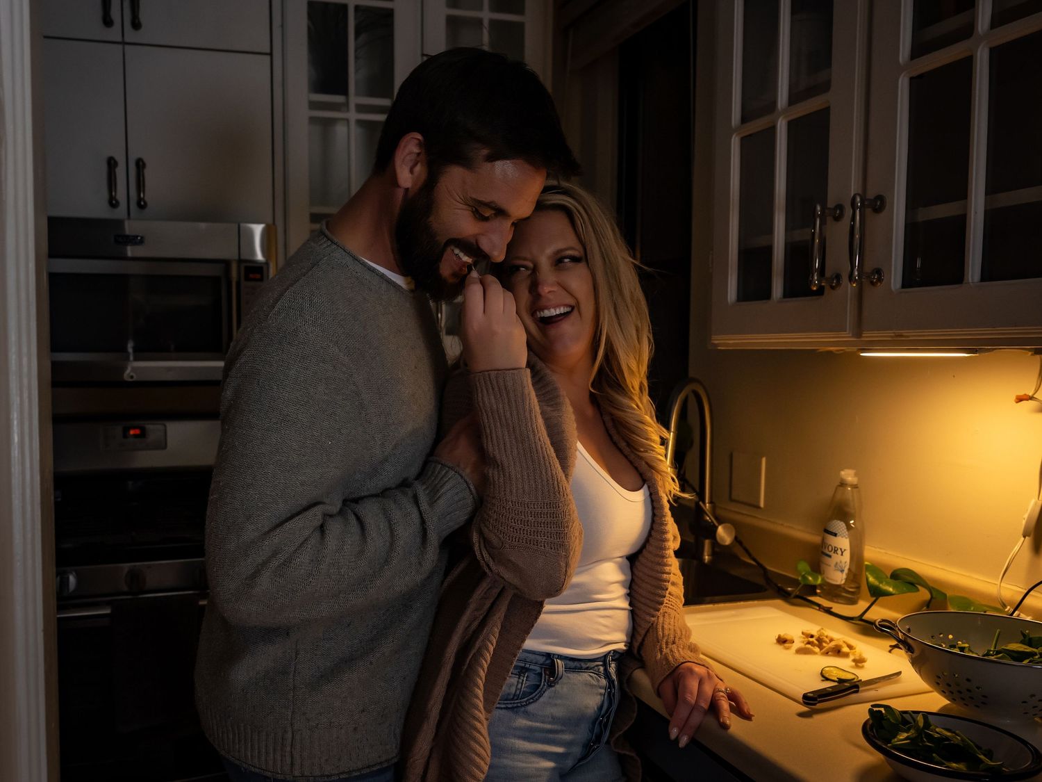 Couple sharing an intimate moment while cooking together in a dimly lit kitchen.