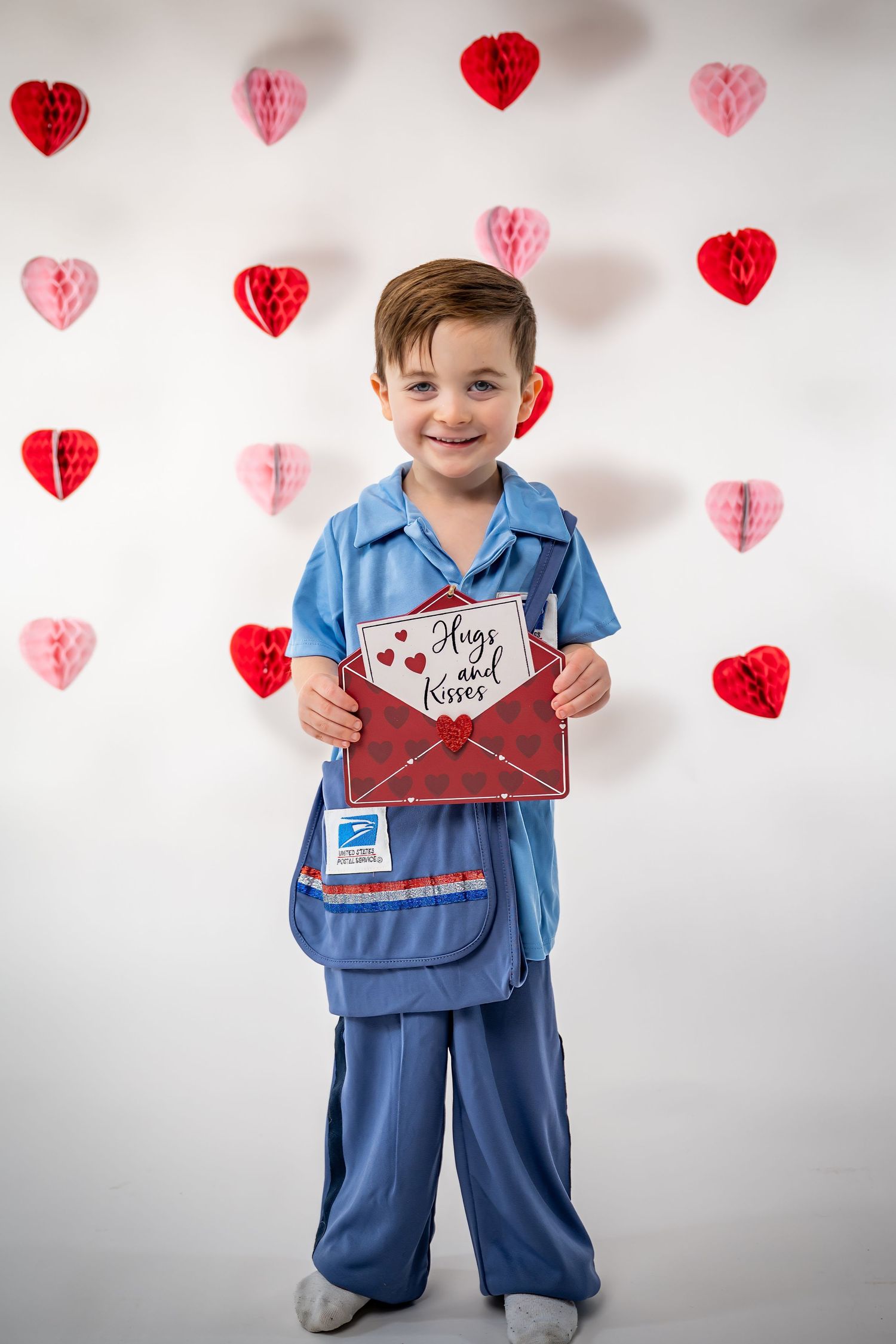 Young child in blue medical scrubs costume holding Valentine card against heart decorated background.