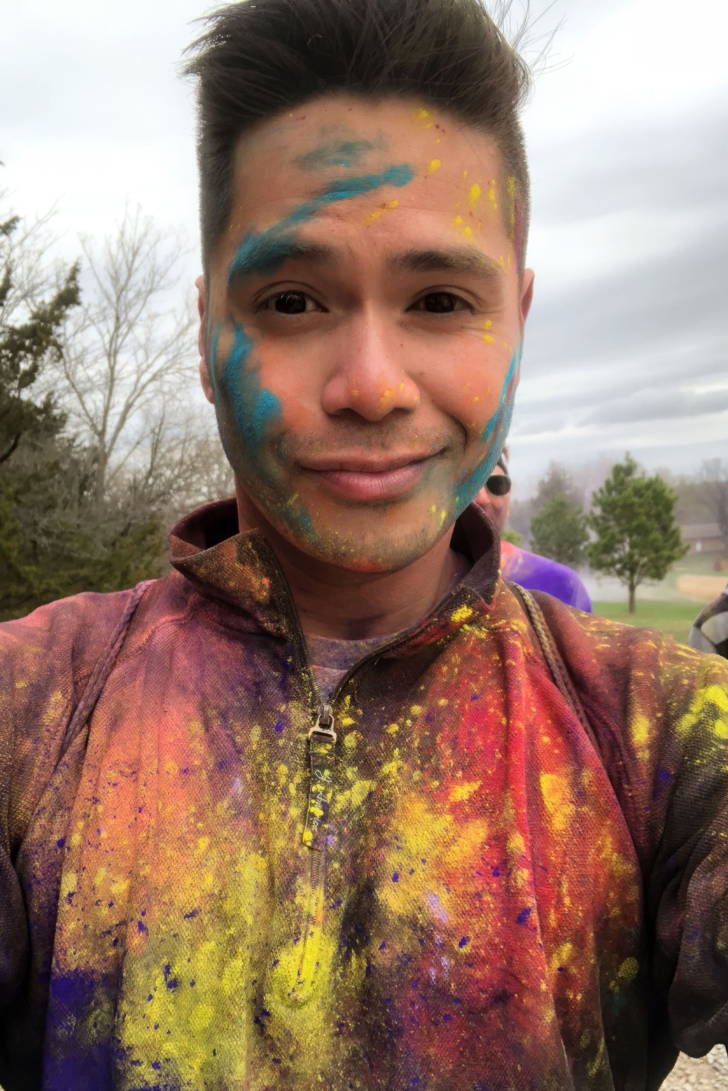 A series of selfies showing a person with colorful powder paint on their face in vibrant rainbow hues during a festival celebration.