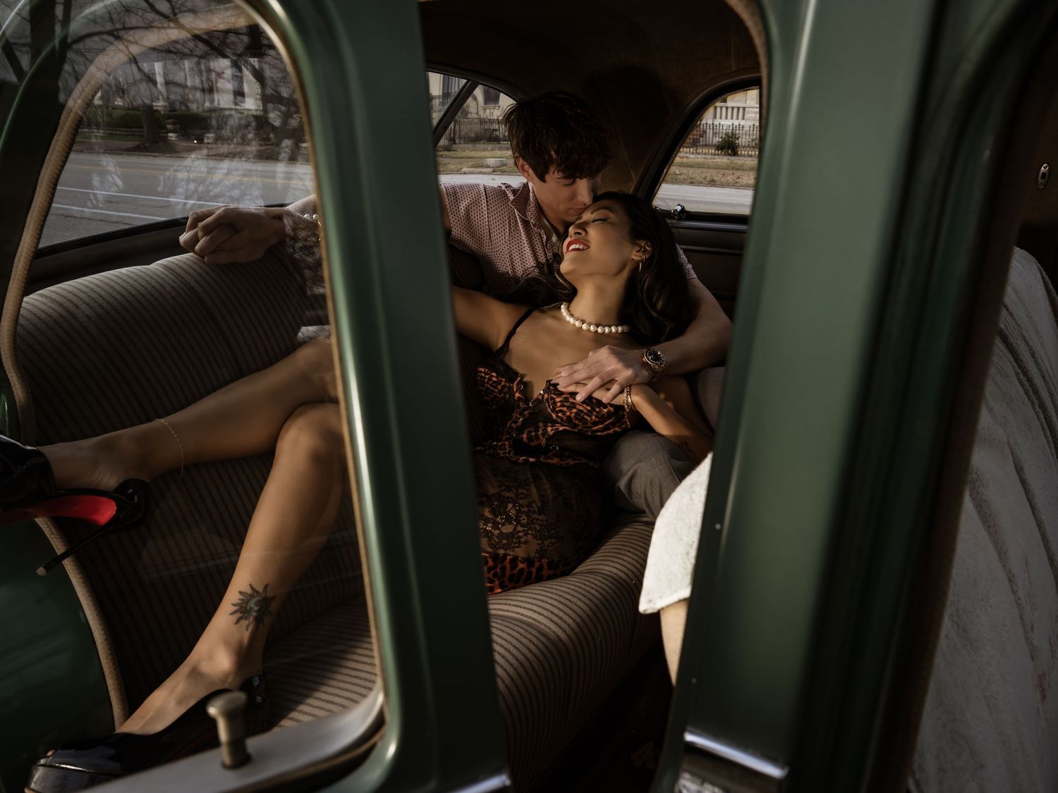 Couple sharing a romantic moment in a vintage car backseat, woman in leopard dress with heels, soft warm lighting.