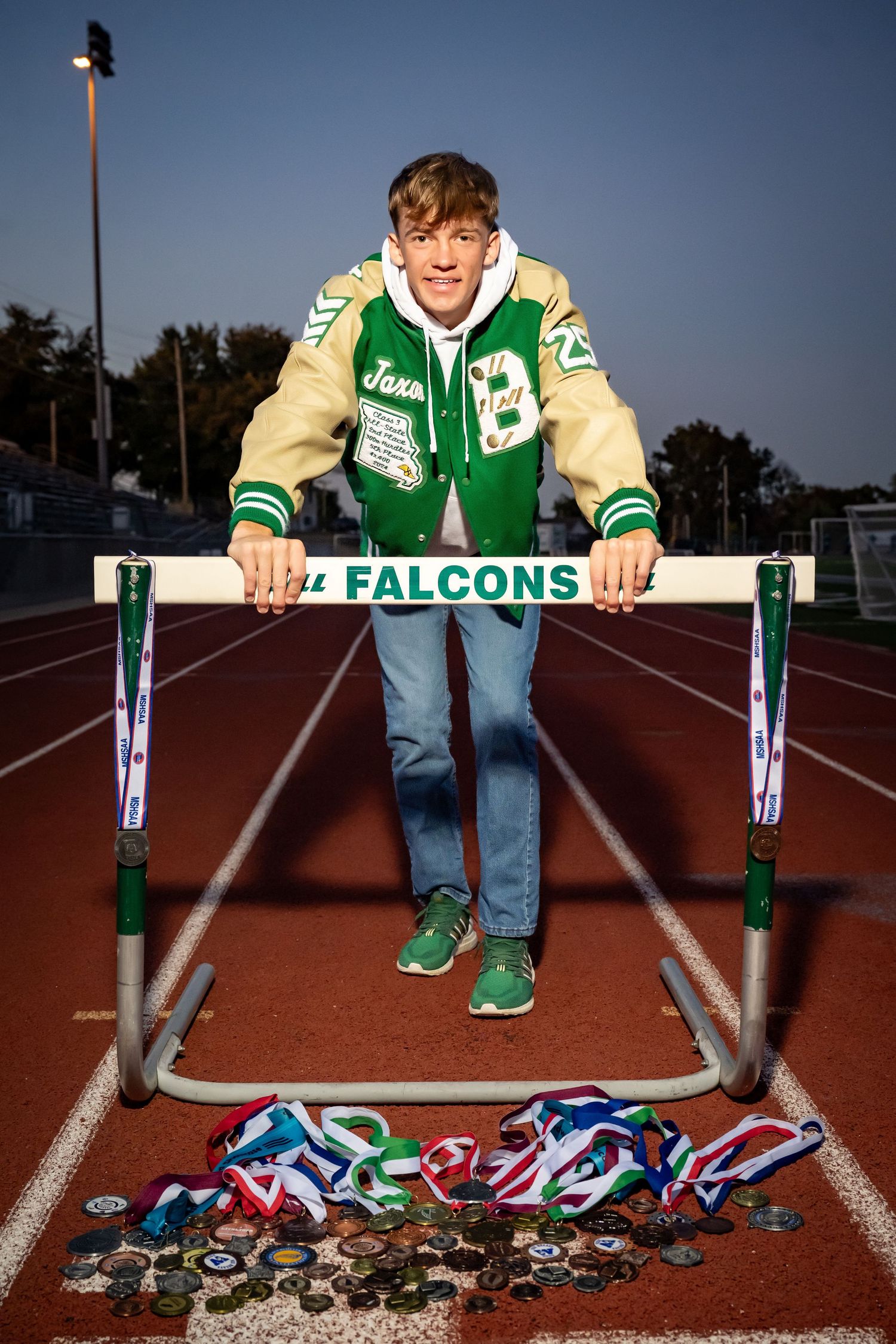 Athletic memorabilia and medals displayed on track surface with green and white varsity jacket.
