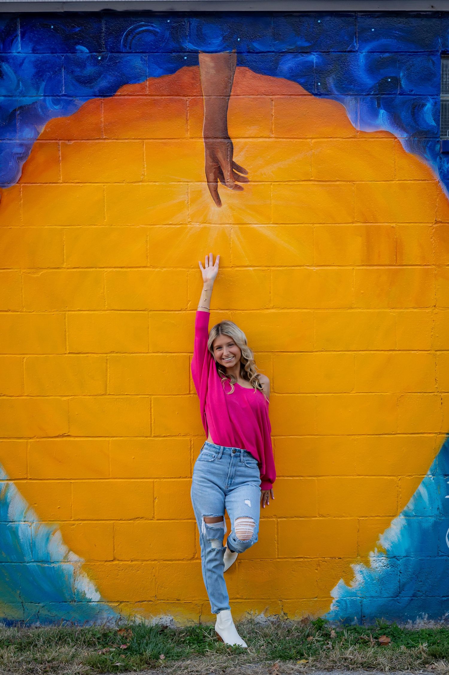 Casual portrait series against vibrant orange and blue painted wall wearing pink sweater and jeans.