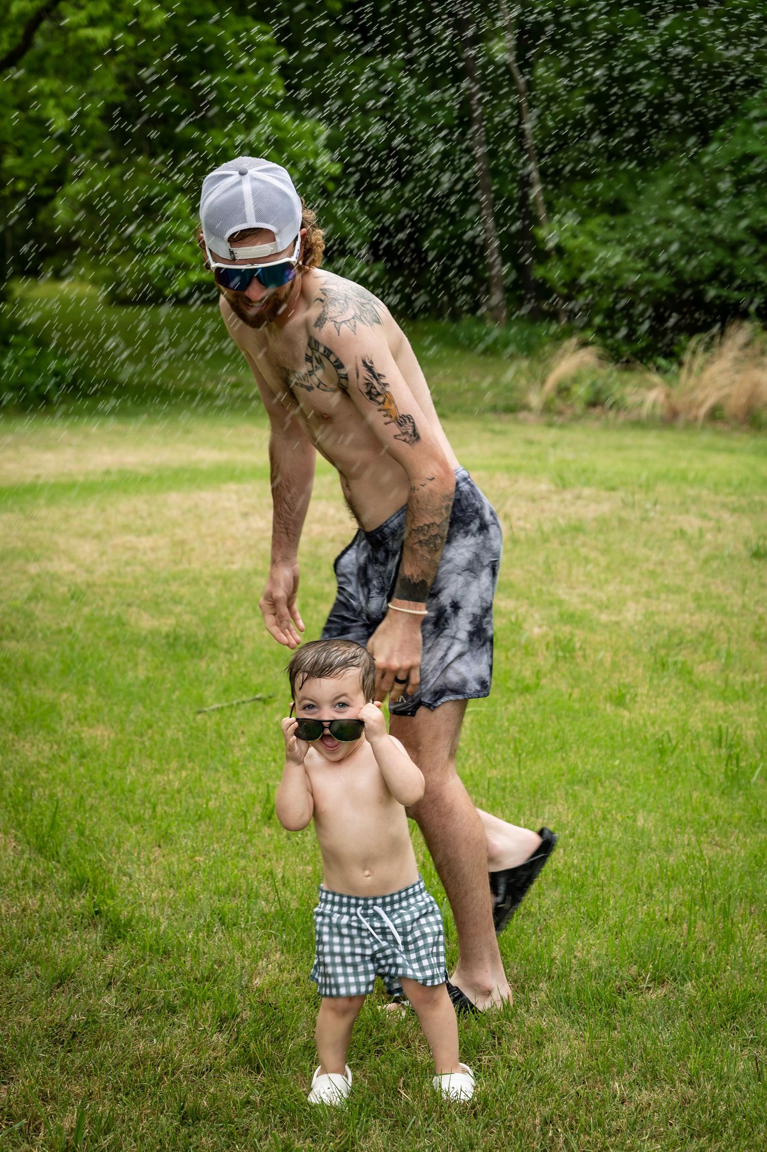 Playing in summer sprinkler on grassy lawn wearing swim shorts.