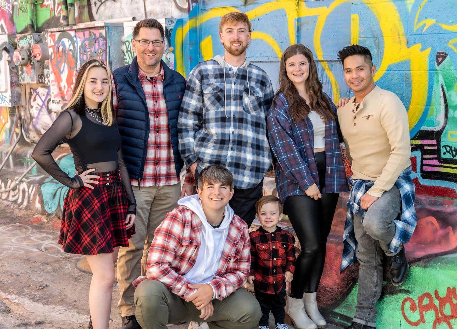Group photo of people posing against colorful graffiti wall with vibrant street art.