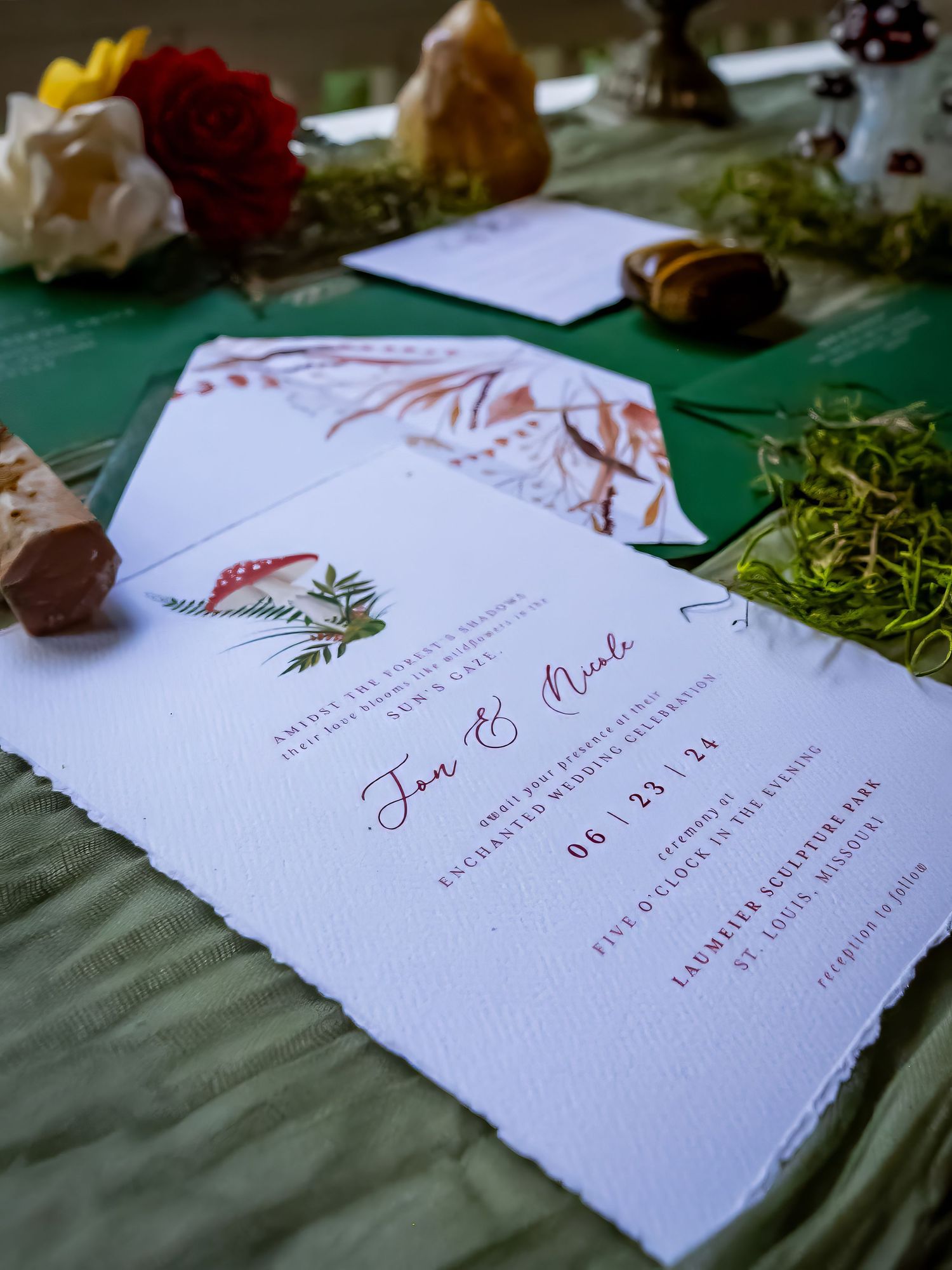Elegant wedding invitations with red floral designs displayed on a green tablecloth.