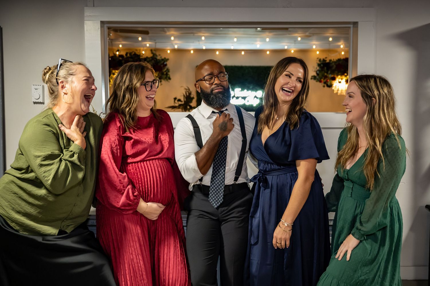Five friends laughing and celebrating together at a festive holiday party, dressed in elegant colorful attire.