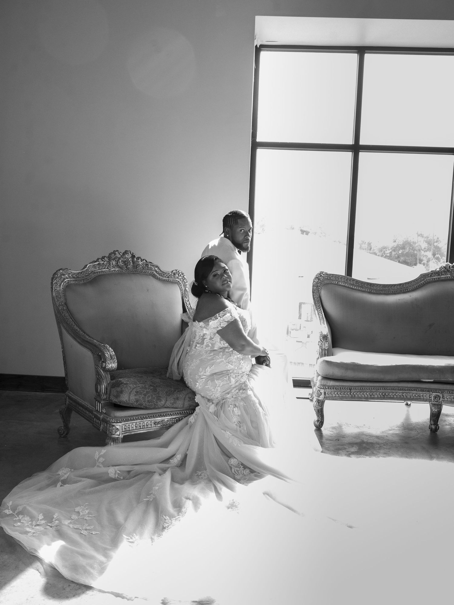 A bride in a white gown poses gracefully near vintage furniture in a bright room.
