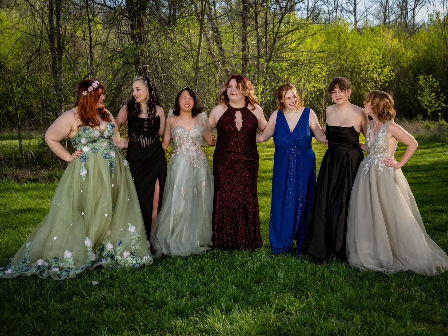 Wedding party group photo with people wearing various colored dresses in a green spring setting.