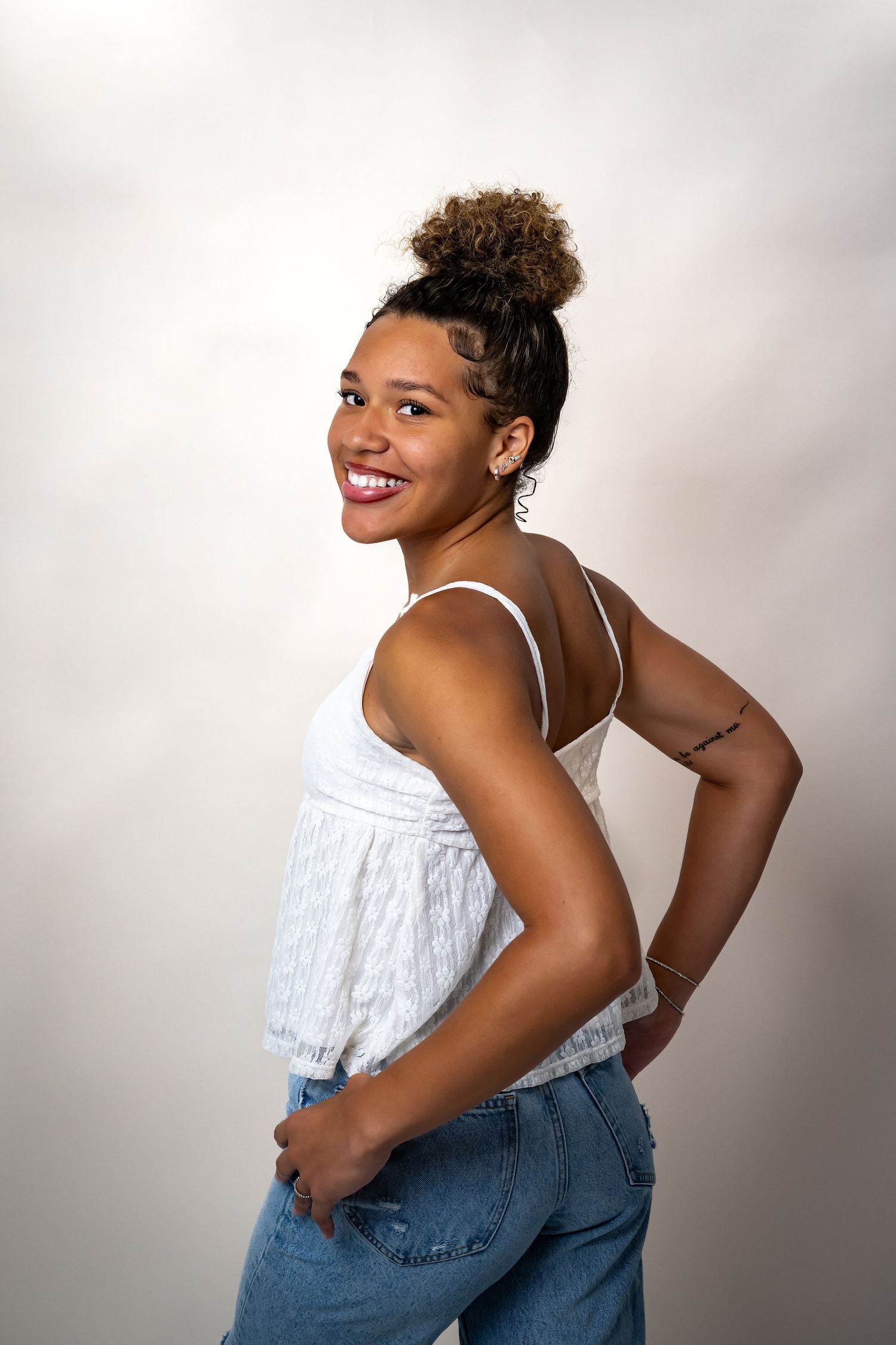 Portrait of a smiling woman in white top and jeans posing against a light background.