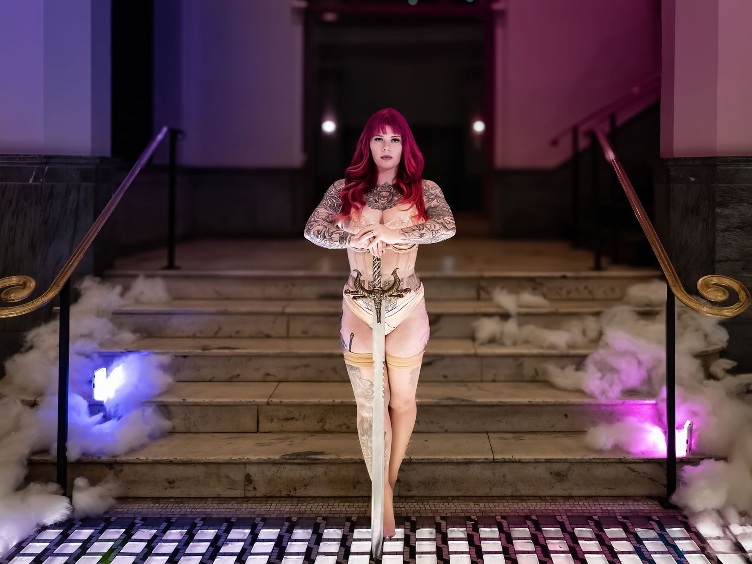 Fashion models walk down a dimly lit runway with purple lighting effects in an evening show presentation.