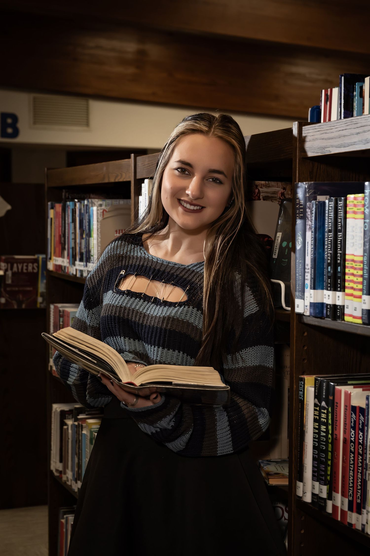 Person reading book in cozy library setting wearing dark knit sweater.