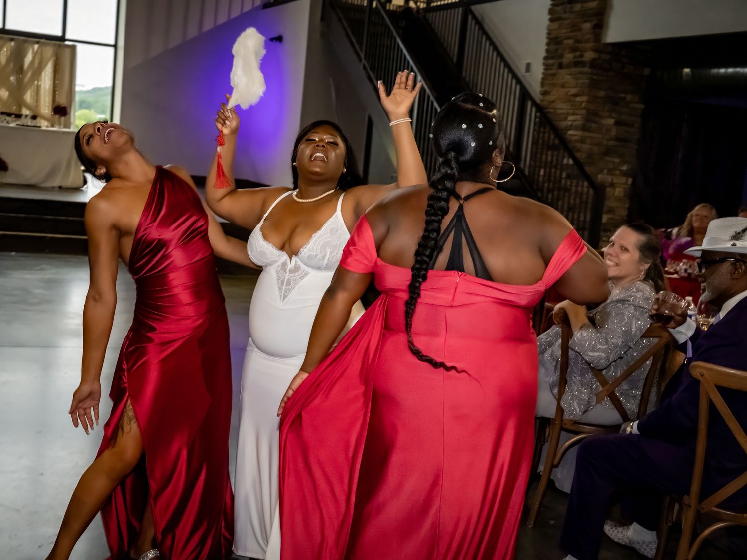 Wedding party members in red dresses dance and celebrate at the reception.