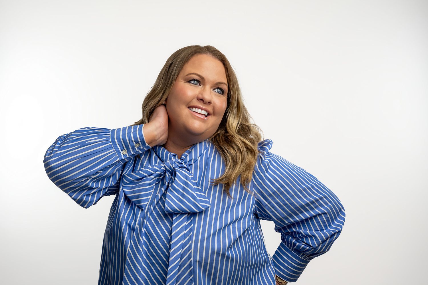 Woman in blue striped bow blouse posing confidently on white background.