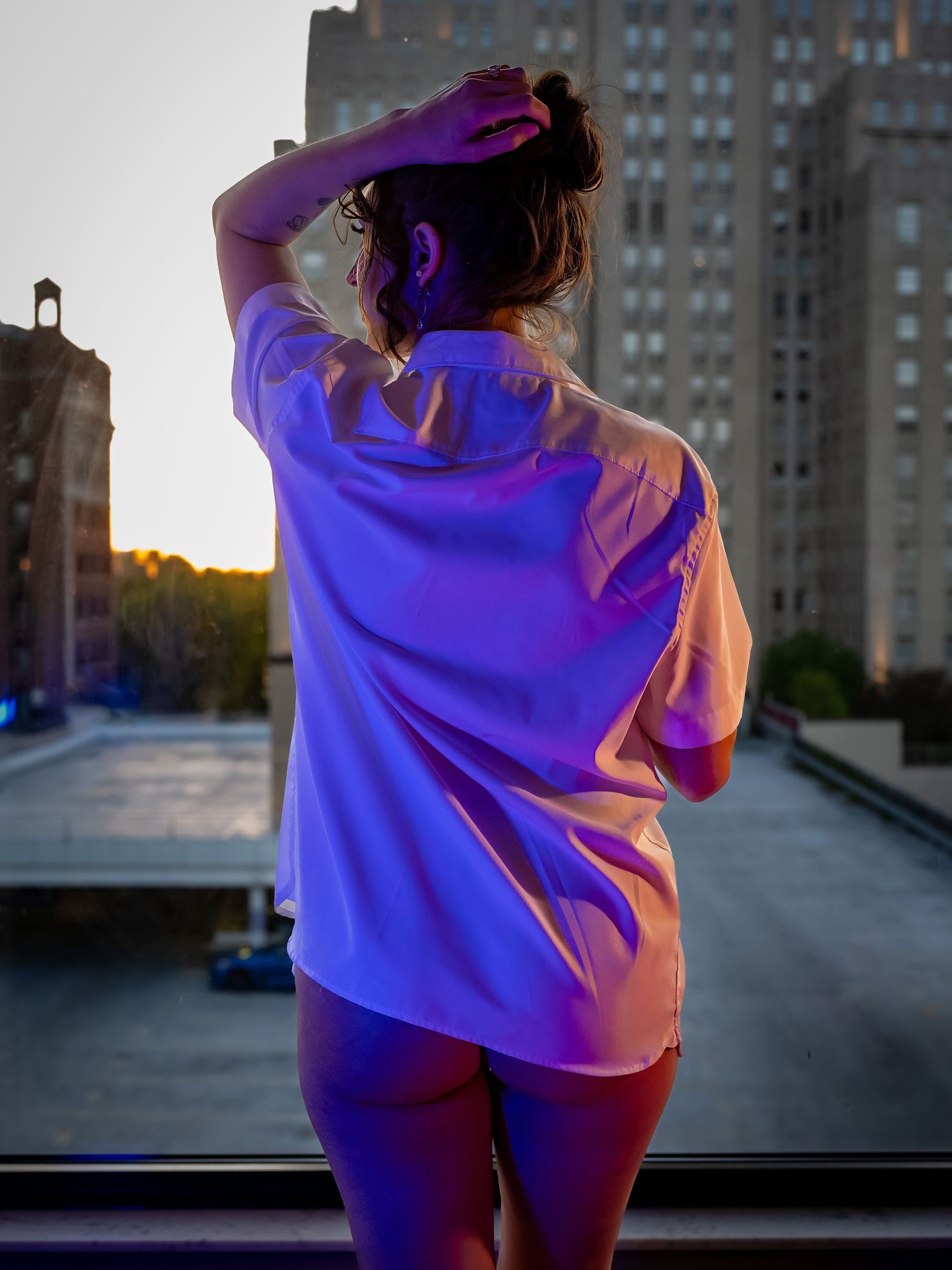 Silhouette against city skyline at sunset wearing loose shirt.
