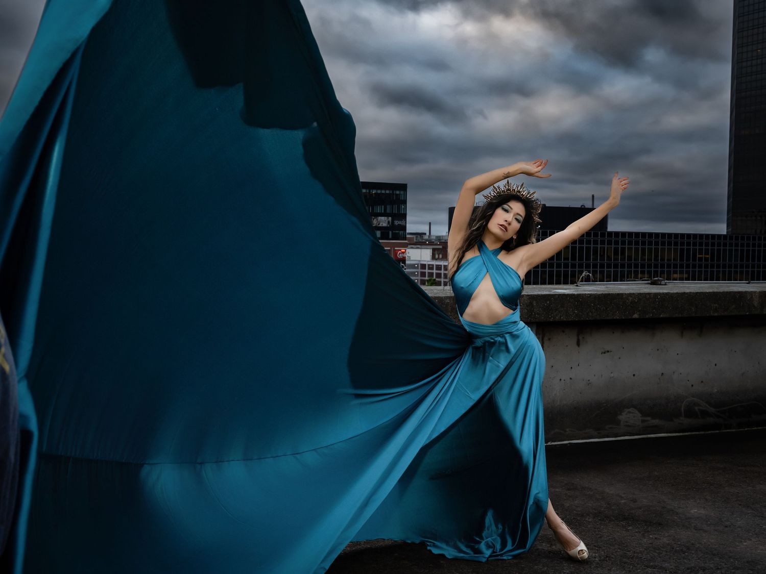 A dancer in a flowing blue dress performs graceful movements against a dramatic cloudy sky background.