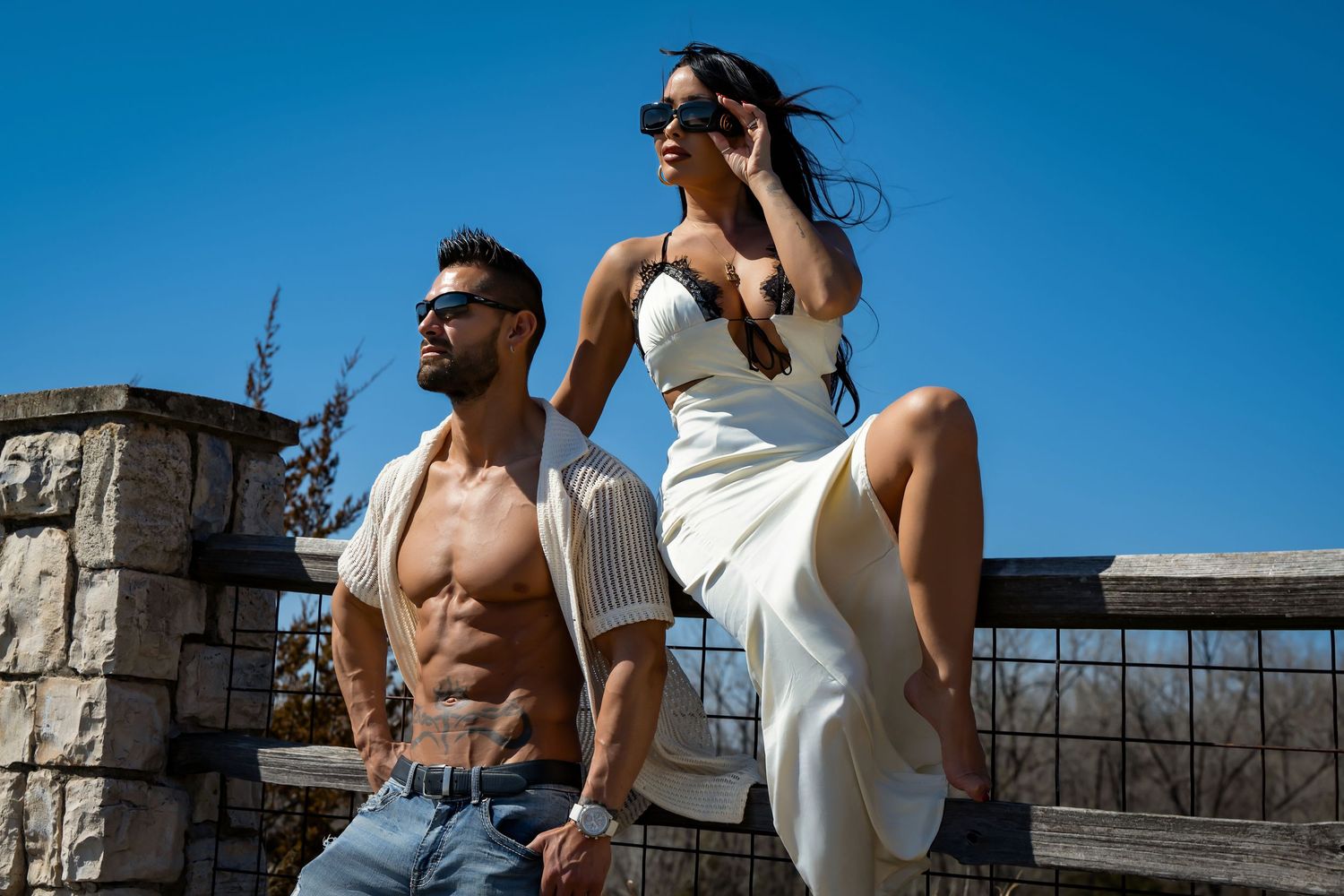 Athletic couple in casual wear posing against blue sky backdrop during outdoor photoshoot.