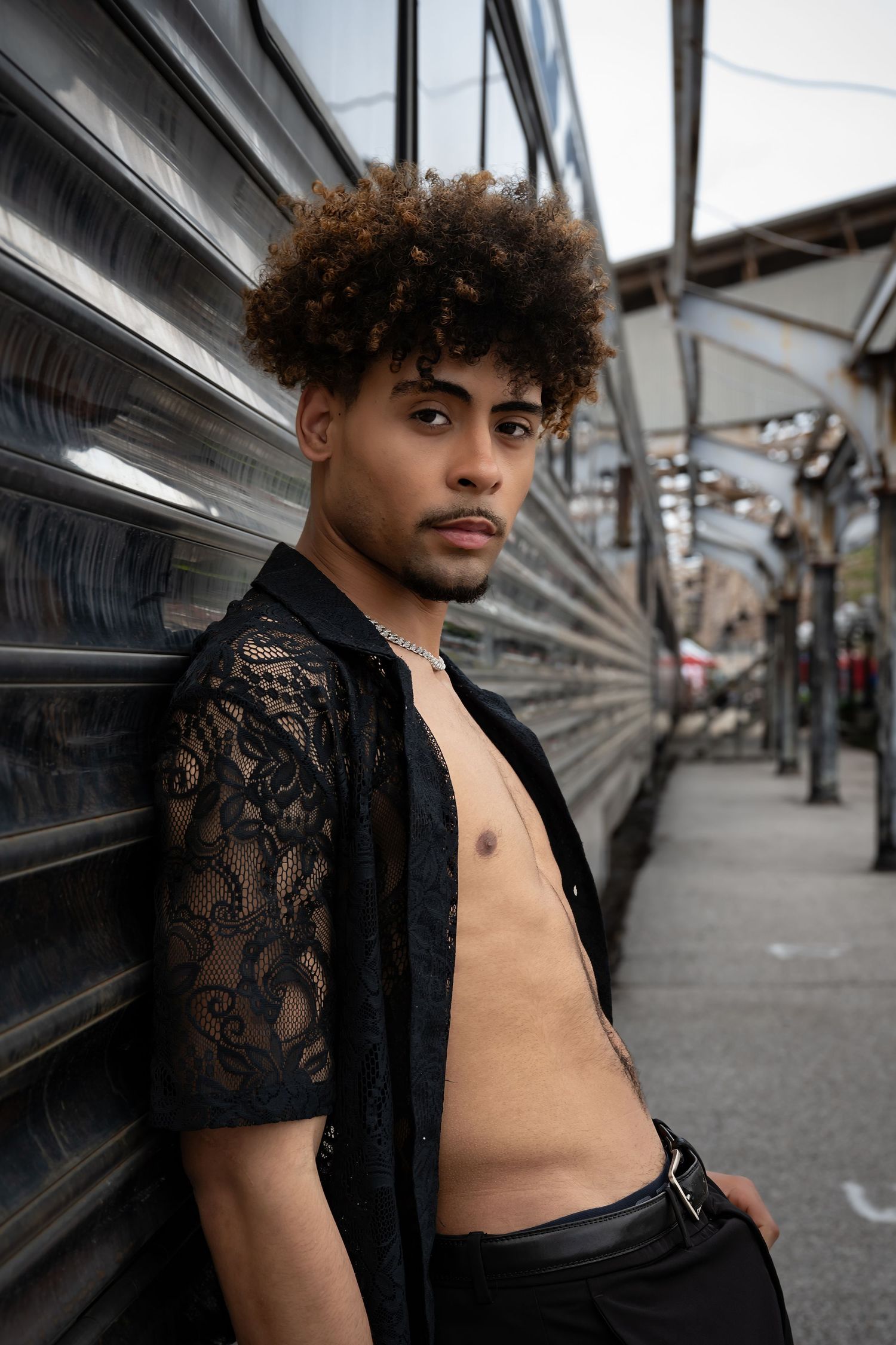 Person in black lace top posing against metallic background on urban street.