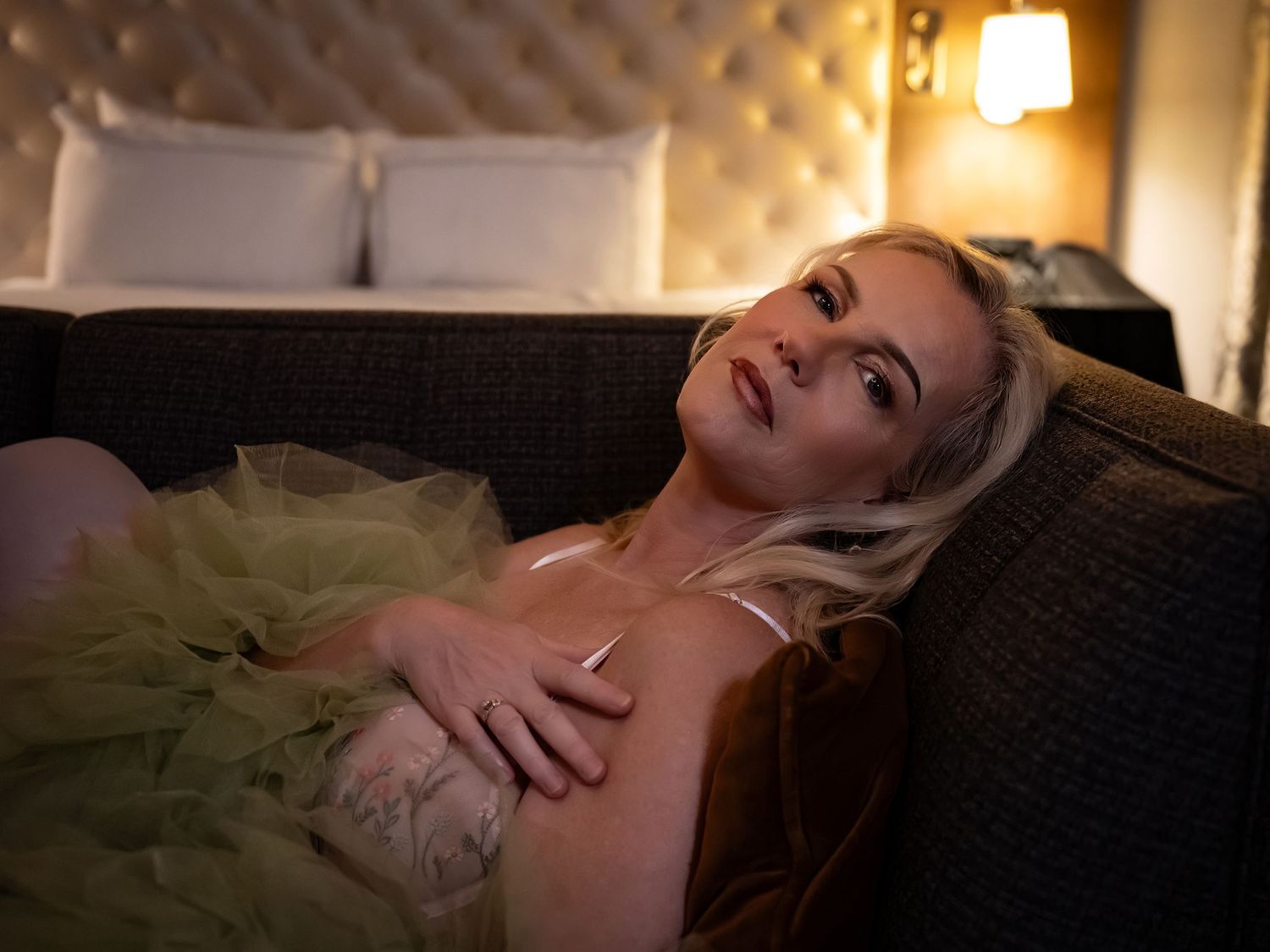 A person lies on a dark couch in a dimly lit room with warm ambient lighting creating a moody atmosphere.