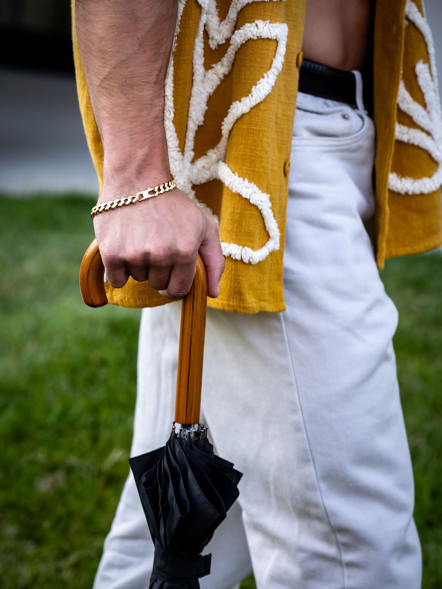 Close-up of hand holding black umbrella with mustard yellow and white clothing.